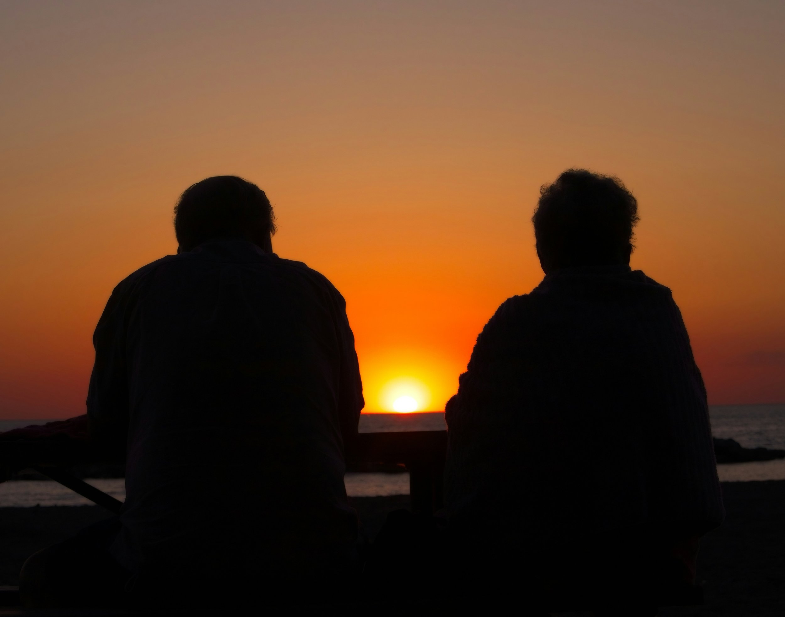 Two people sitting on a beach watching a sunset.