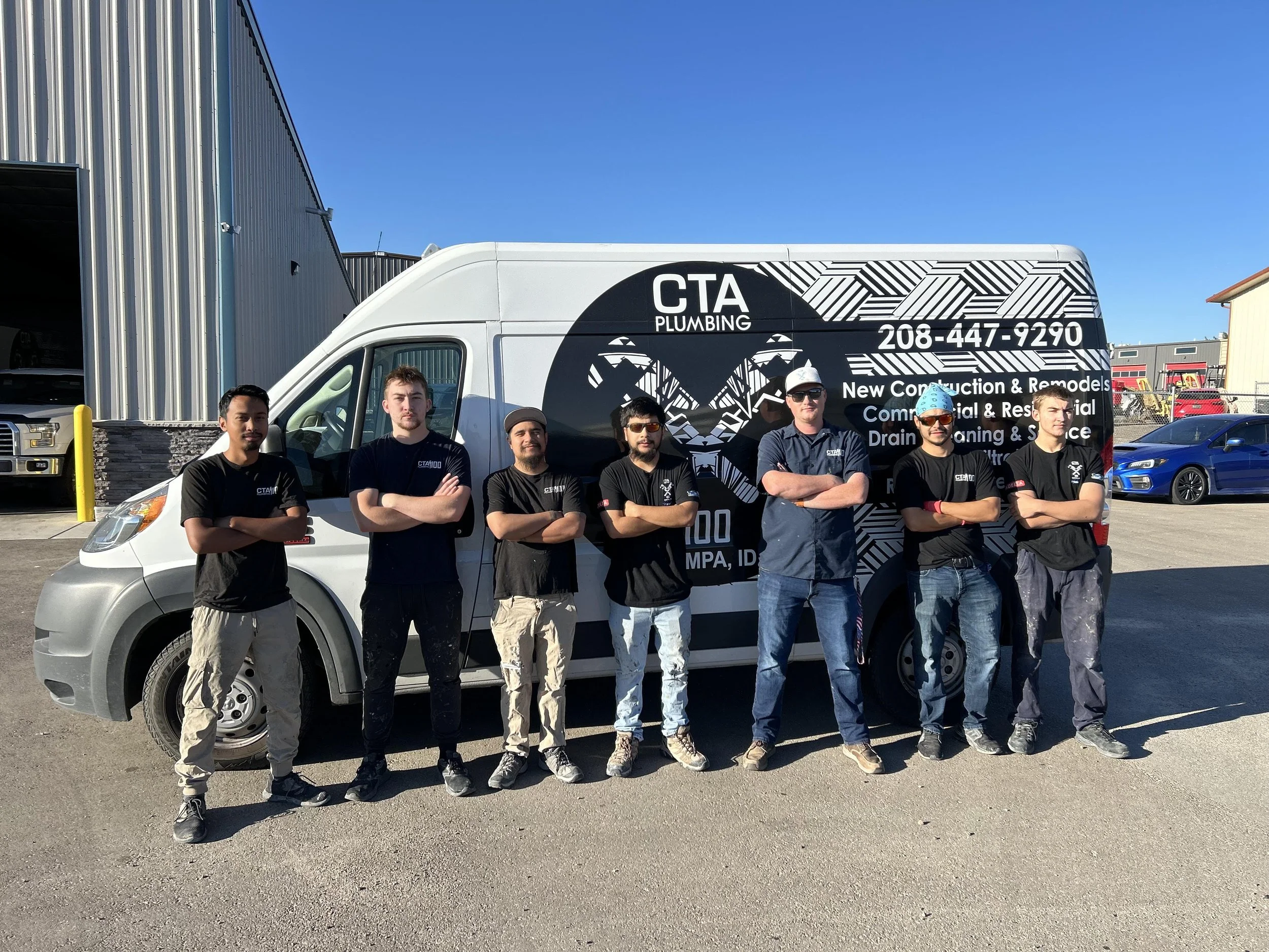 Group of seven employees standing with arms crossed in front of a CTA Plumbing service van in a parking lot.