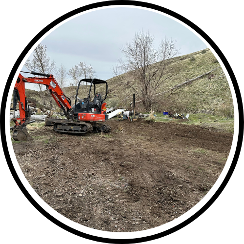 A small red and black excavator on a dirt construction site with a hill and some leafless trees in the background.