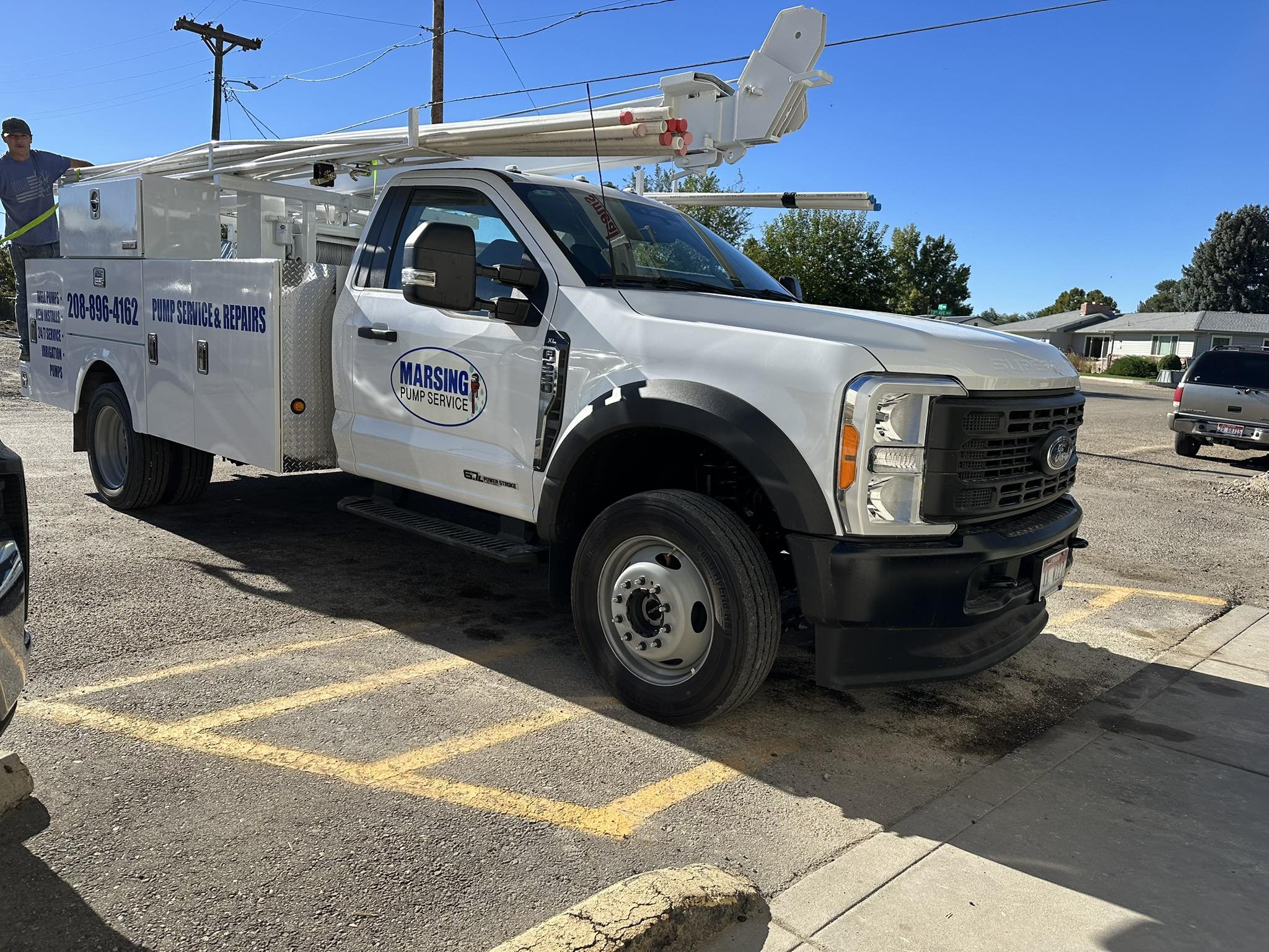 Service truck labeled 'Marsing Pump Service' with a ladder on top, stationed in a parking lot on a sunny day.