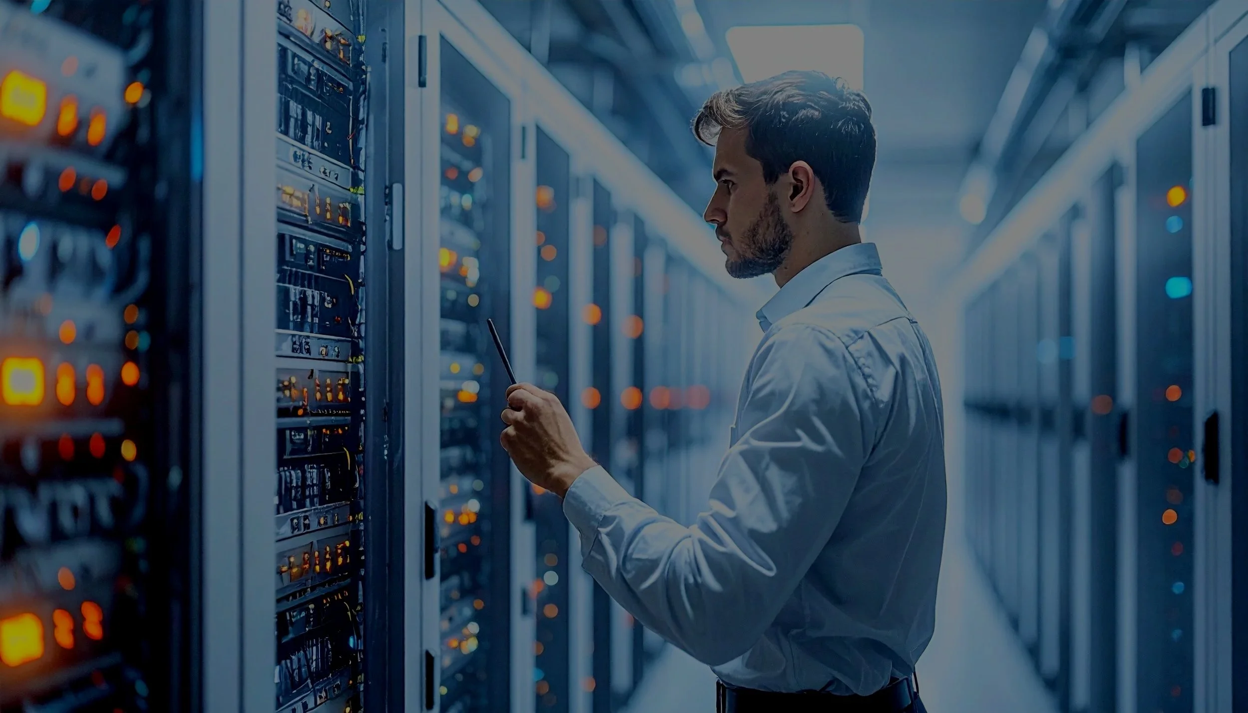 A man in a white shirt working in a server room, holding a tablet and inspecting servers with numerous glowing lights.