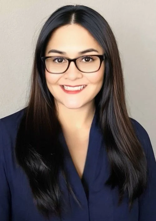 A woman with long dark hair, glasses, and a navy blue top, smiling at the camera against a plain background.