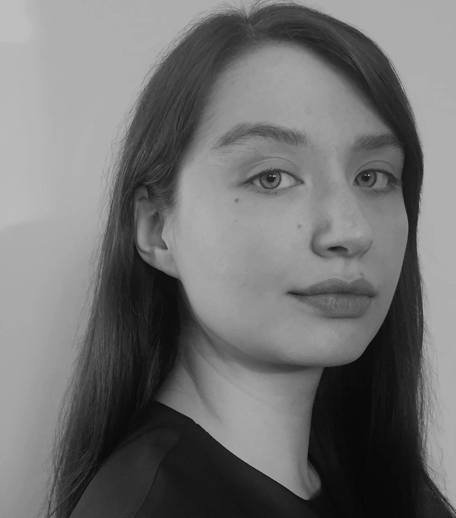 Black-and-white portrait of a young woman with long dark hair, light eyes, and full lips, facing slightly to the right, against a plain background.