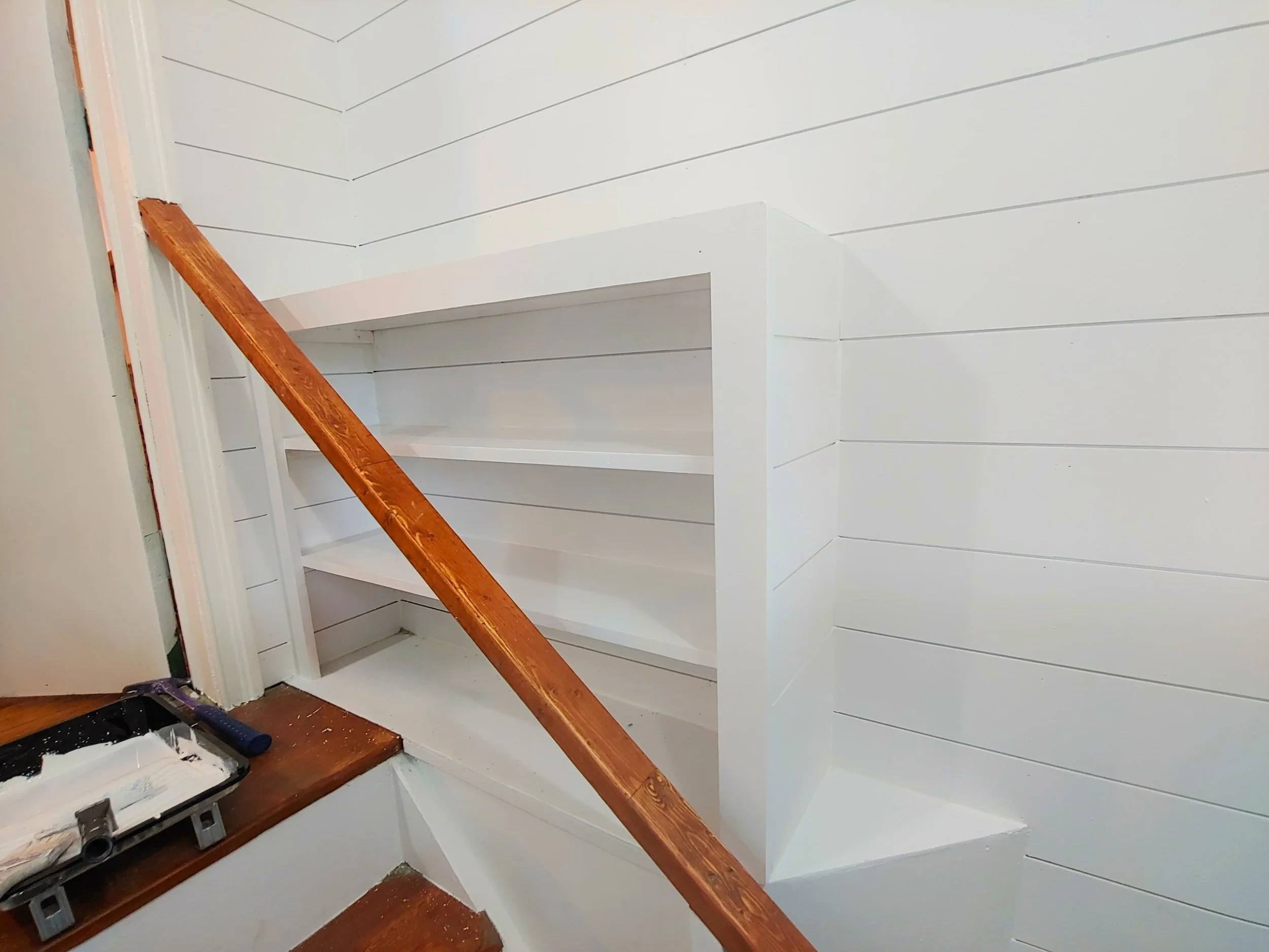 White built-in shelves and wood railing in a home interior under construction.