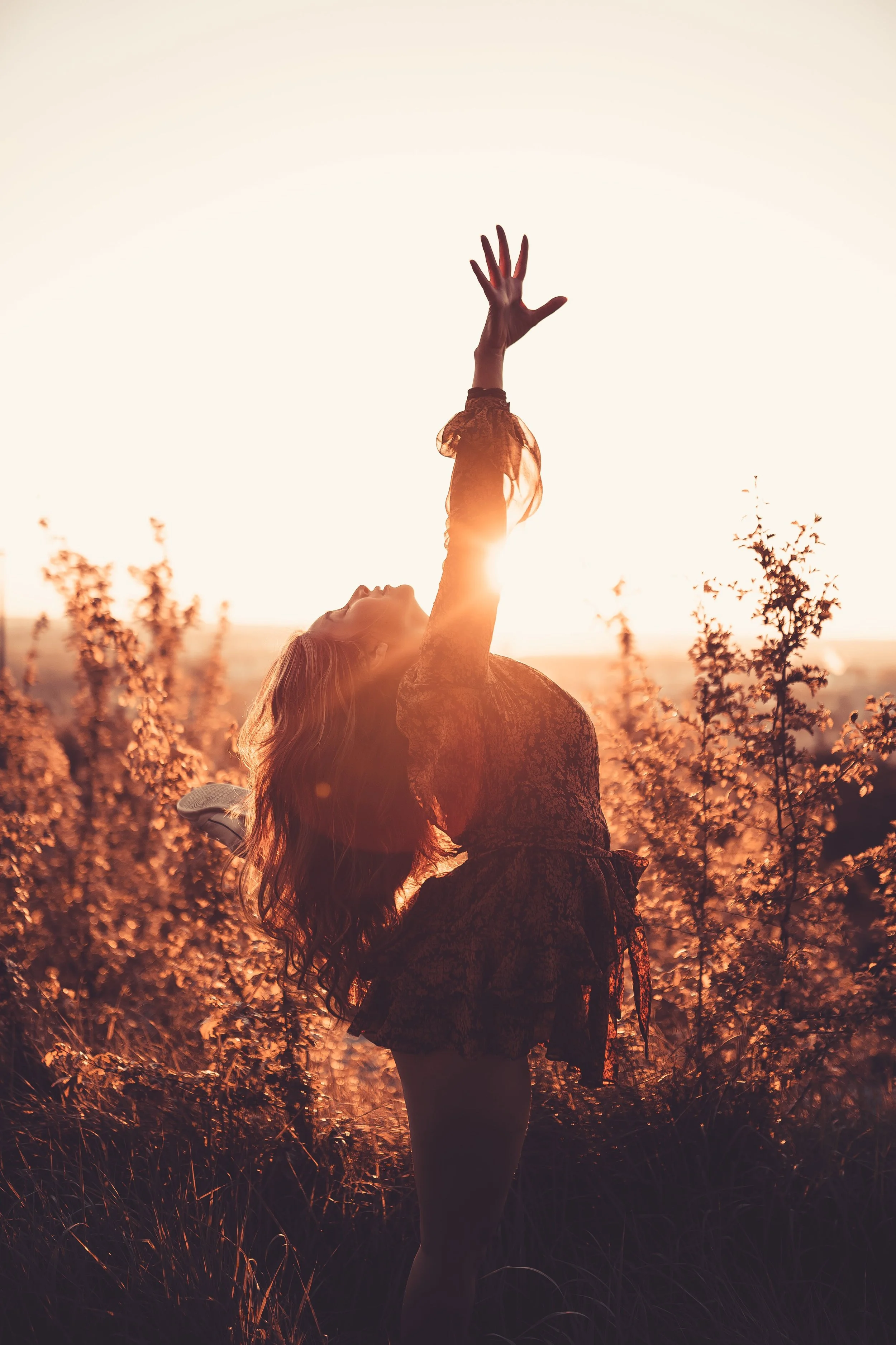 A woman in a field leaning back and reaching for the sky