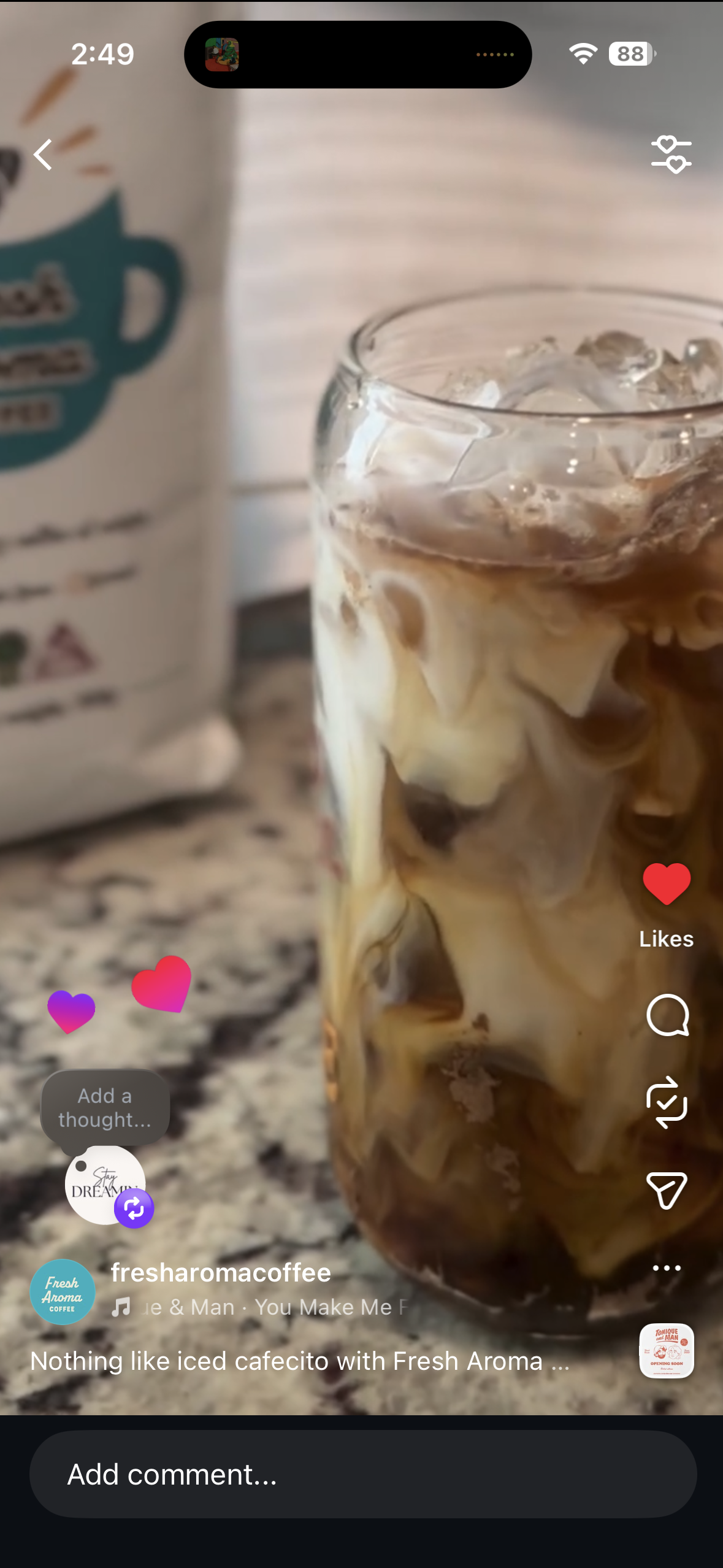 A glass of iced coffee with cream swirled in, on a speckled countertop, next to a bag of coffee and a white container.