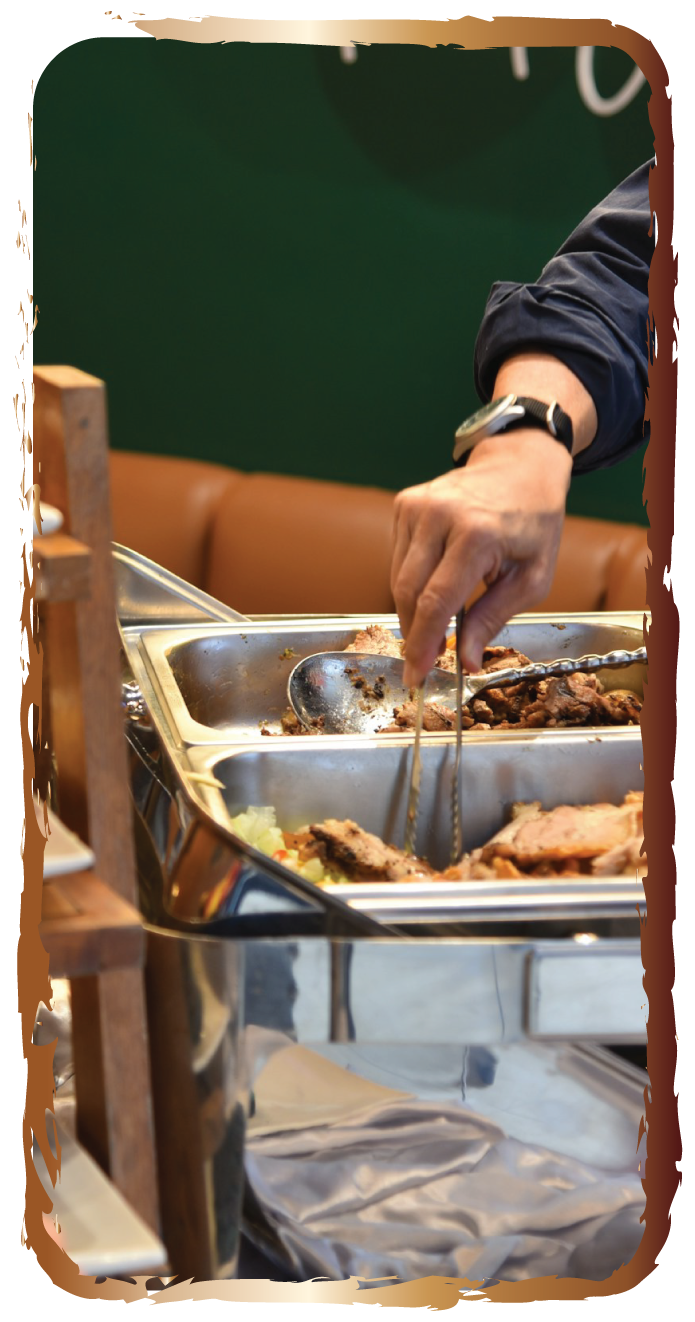 Person serving sliced roasted meat from a stainless steel buffet tray with tongs, in a restaurant setting.