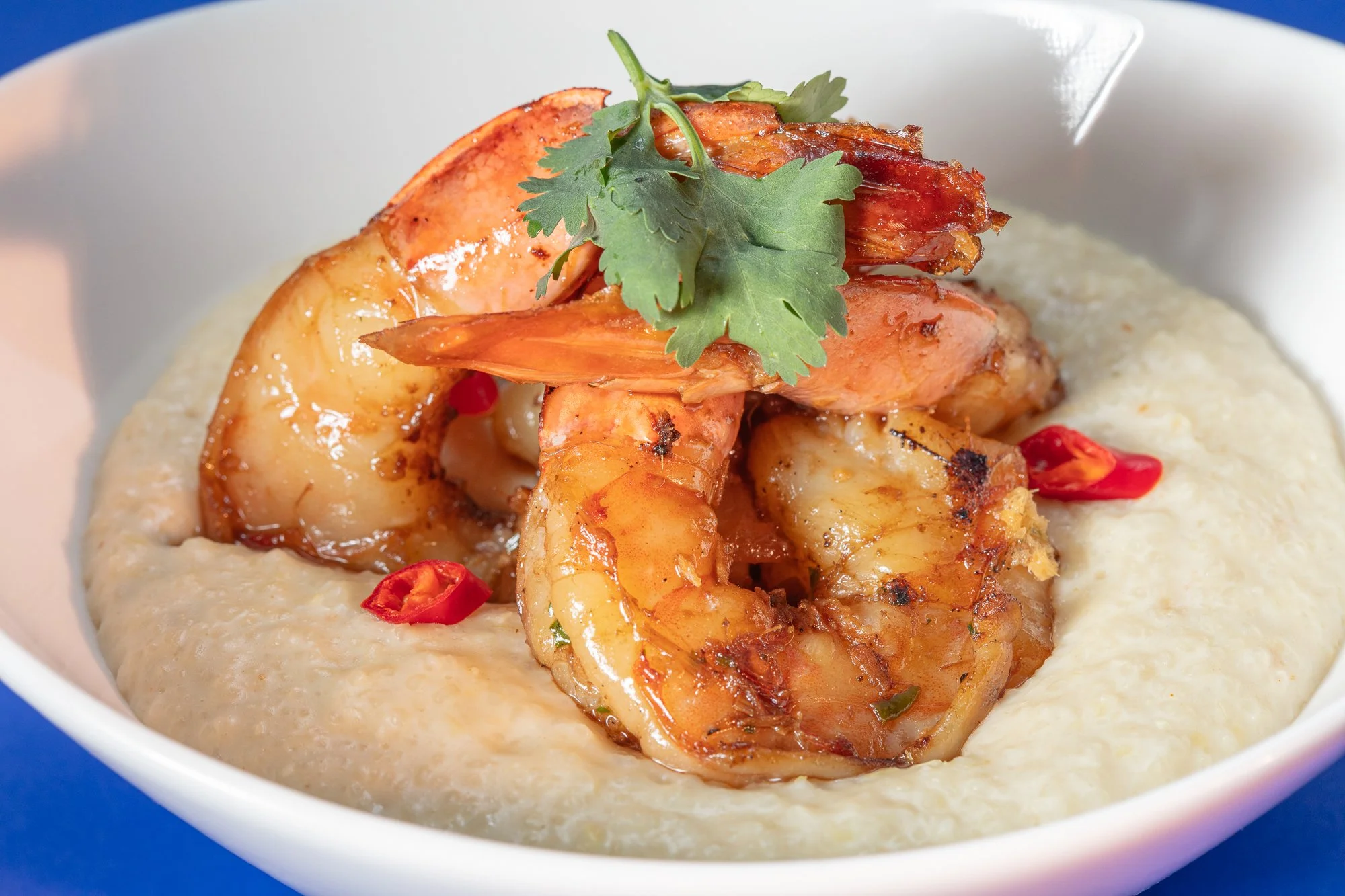 Shrimp served over creamy grits, garnished with red chili slices and fresh cilantro.