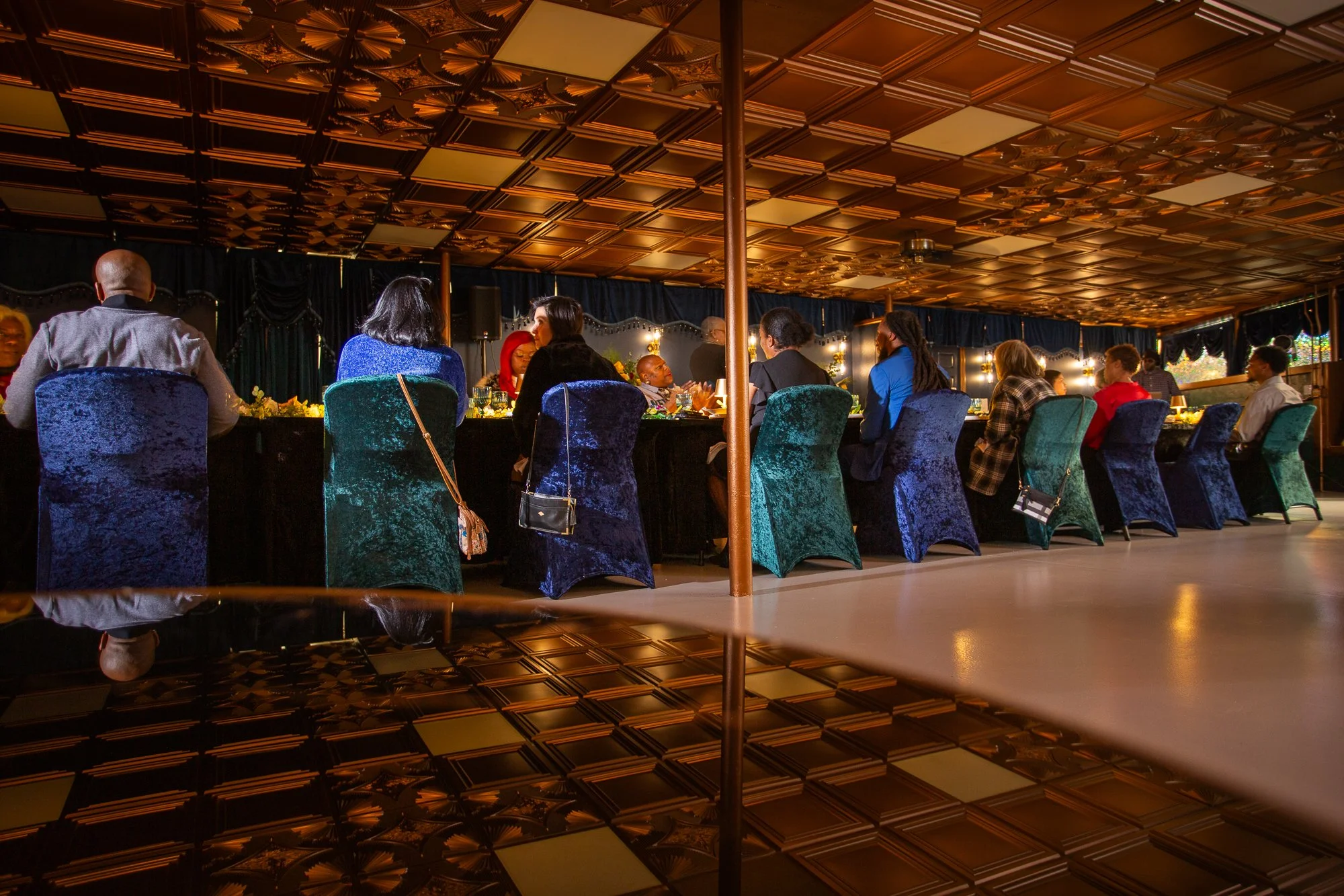 People seated at a long banquet table in an elegant, dimly lit restaurant with a decorative ceiling and dark curtains.