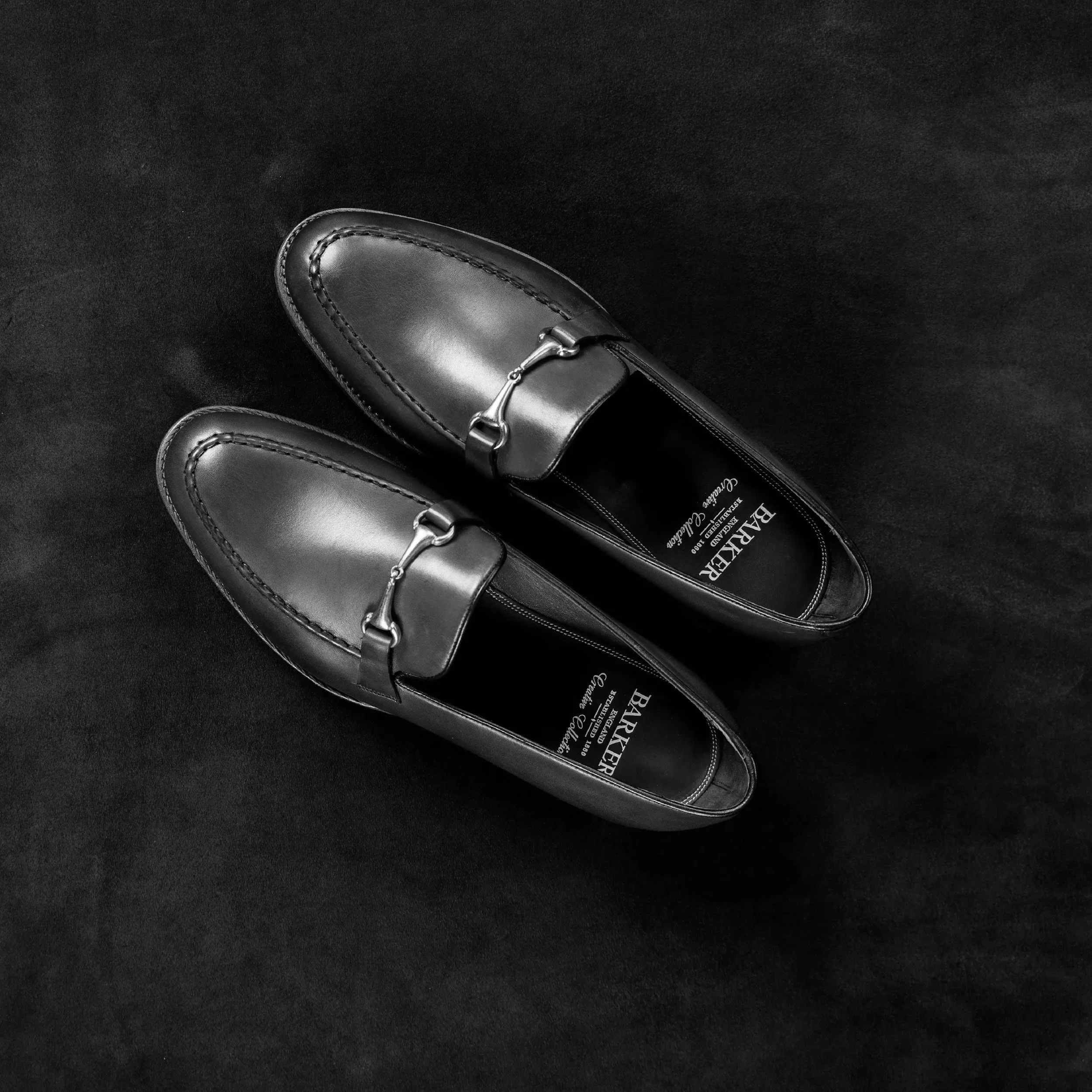 Pair of black leather loafers with metal horsebit detail, placed on a dark surface.
