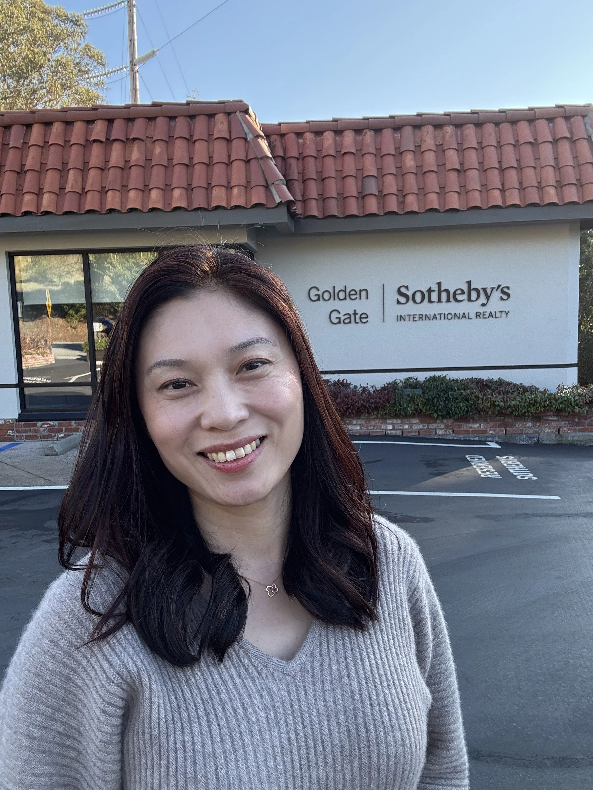 Fang Yuan standing beside the Golden Gate Sotheby’s International Realty sign at the Woodside office.
