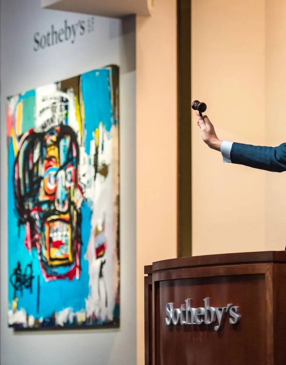 苏富比拍卖行现场，拍卖师举槌，背景为当代艺术作品。