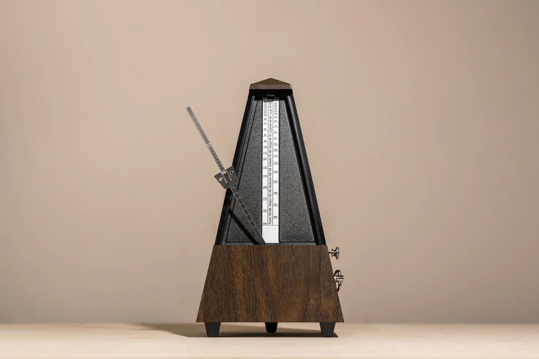 A metronome with a wooden base and black top, featuring a vertical scale and a swinging arm with a sliding weight.
