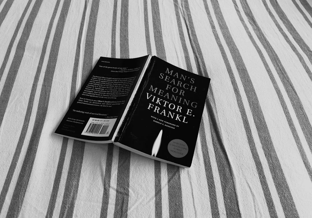 Open book titled 'Man's Search for Meaning' by Viktor E. Frankl resting on a bed with striped sheets.