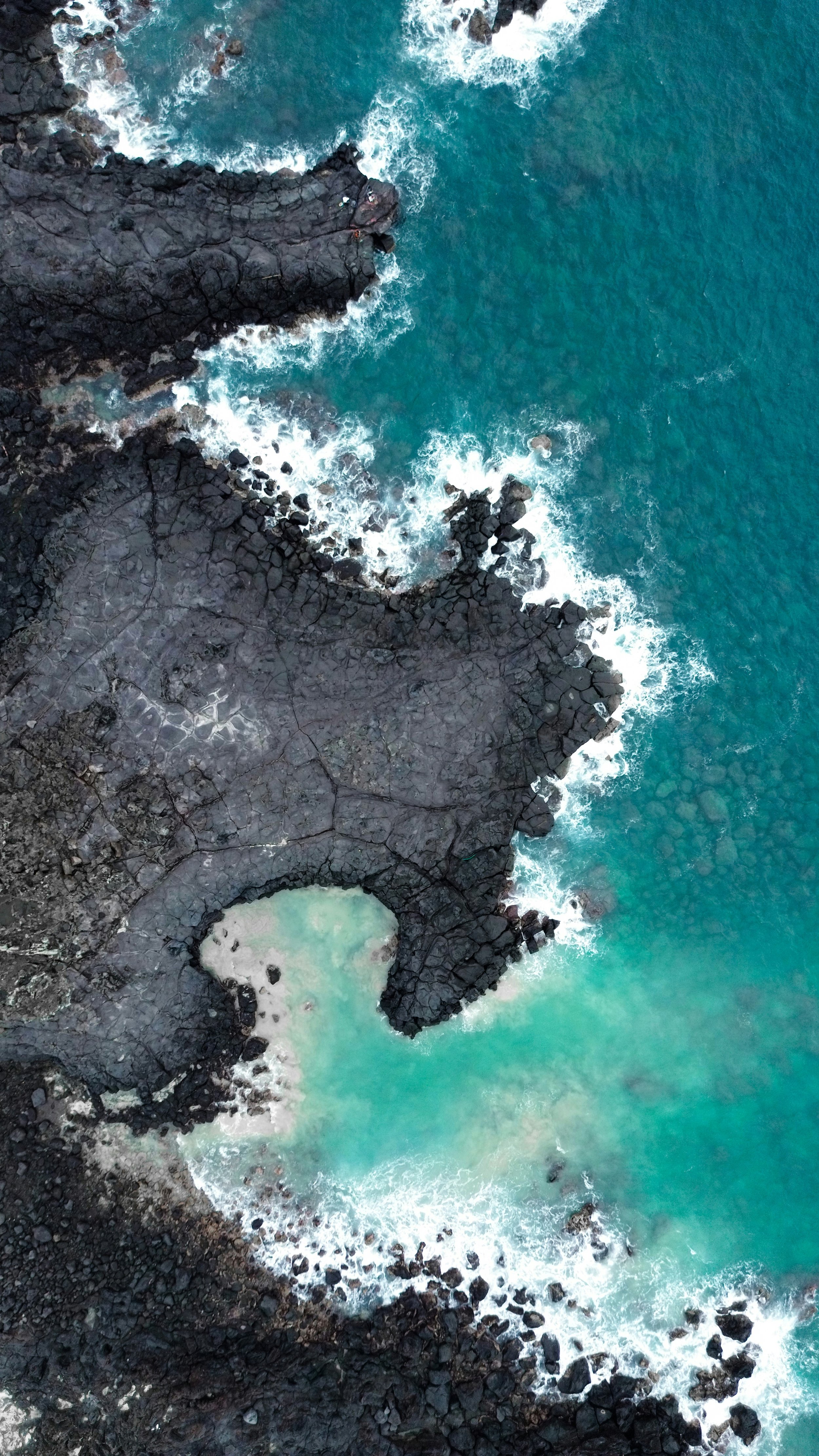 An aerial view of a Hawaiian coastline with dark volcanic rocks and turquoise water.