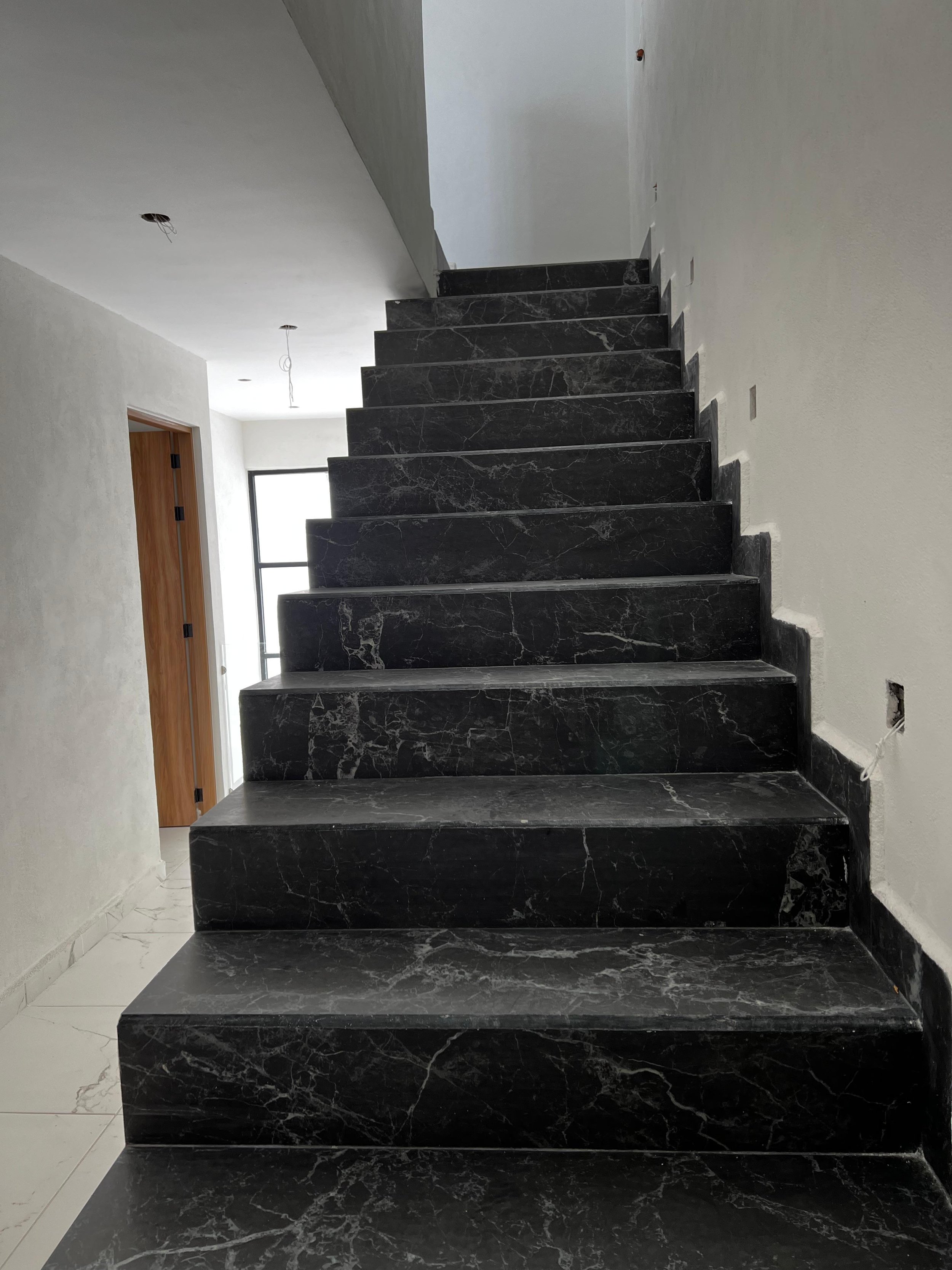 Escalera de mármol negro en interior de casa en construcción.