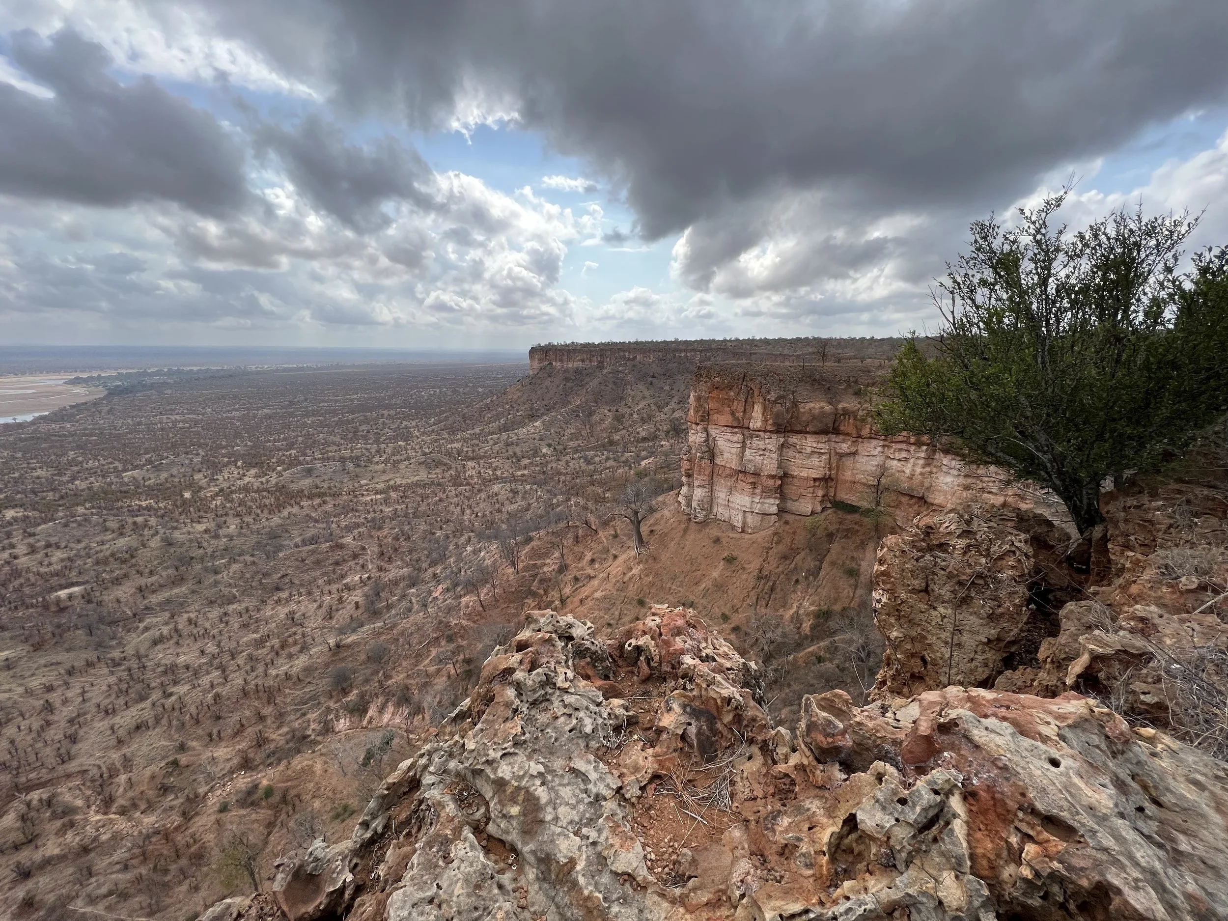 A peaceful landscape featuring a body of water with mountains in the background and trees in the foreground, with a building partially visible on the right side.