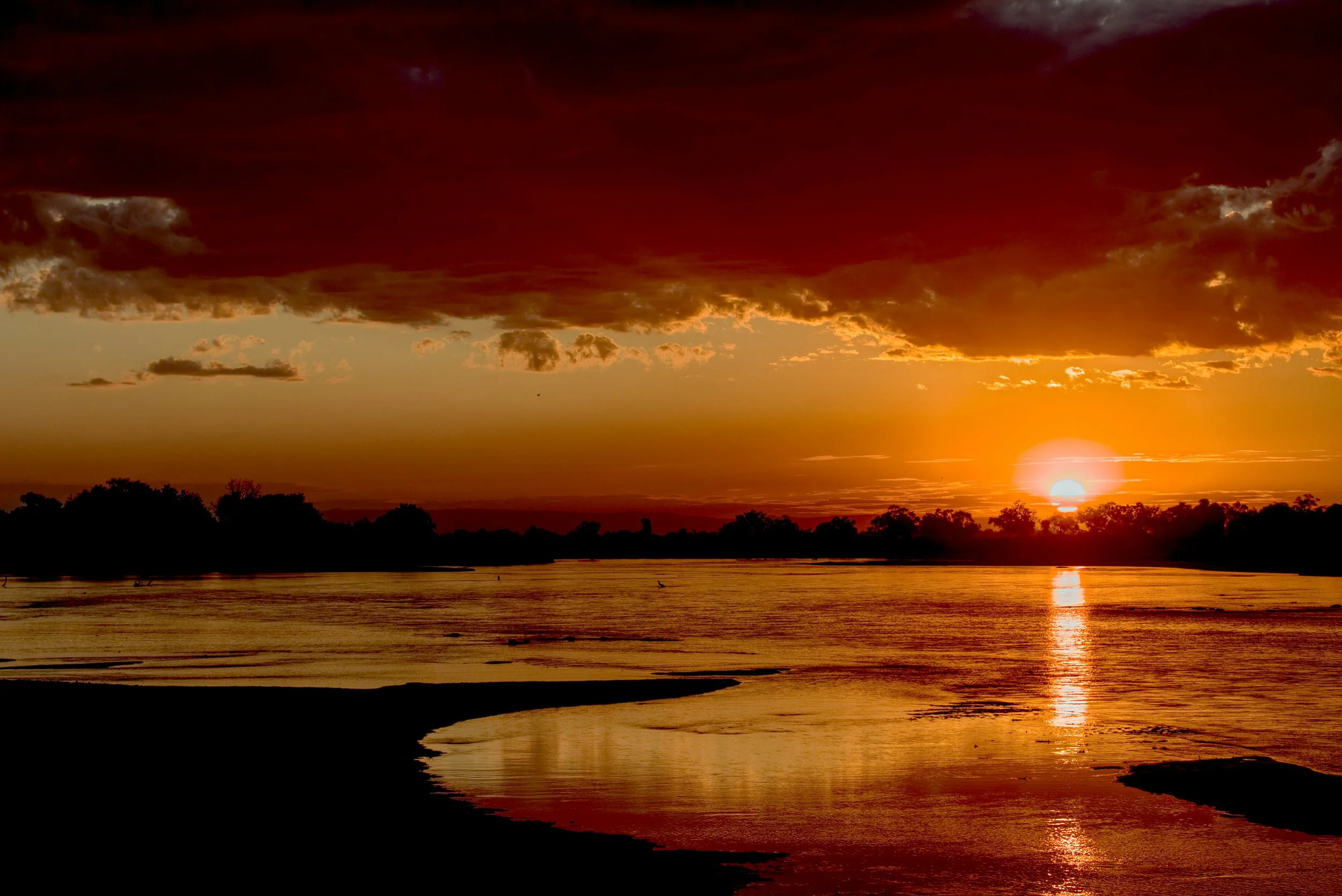 Sunset over a river with dark clouds above, reflecting golden and orange hues on the water