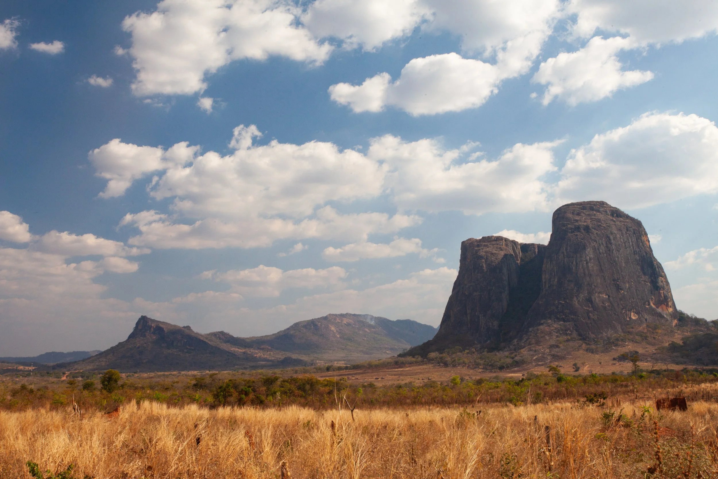 A peaceful landscape featuring a body of water with mountains in the background and trees in the foreground, with a building partially visible on the right side.