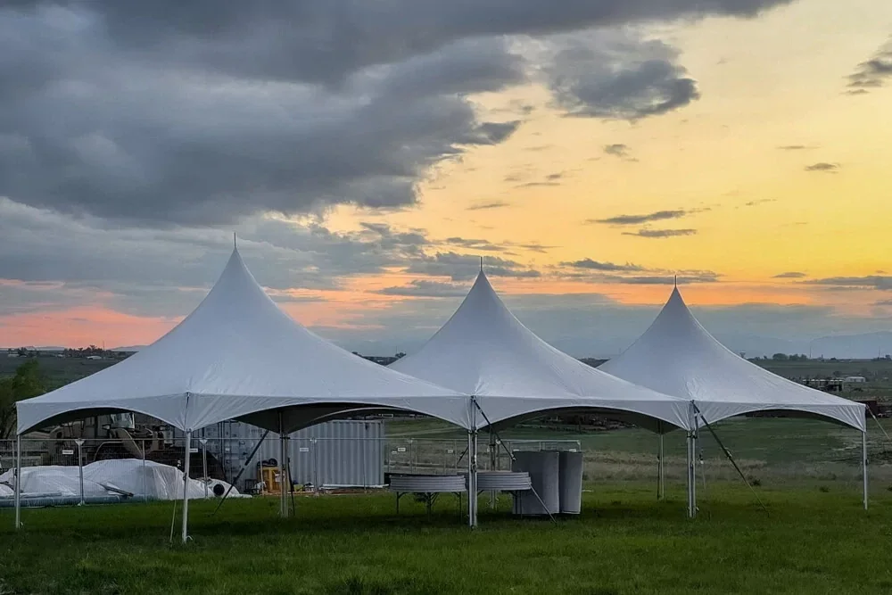 Three white event tents set up outdoors on a grassy field during sunset with dark clouds overhead.