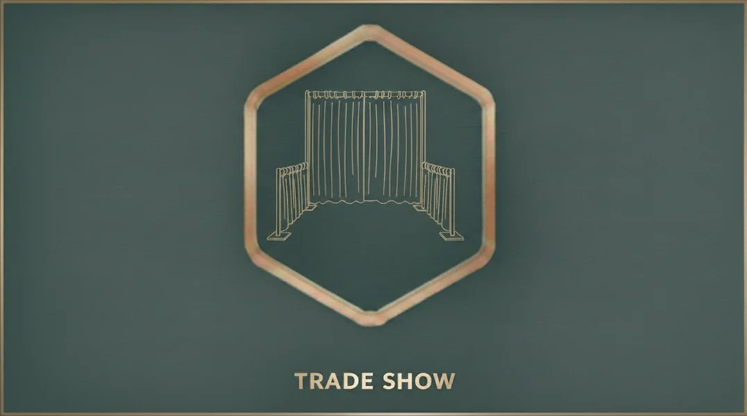 A sign with a gold hexagon border displaying an illustration of curtains and stanchions. Below, the text reads "Trade Show."