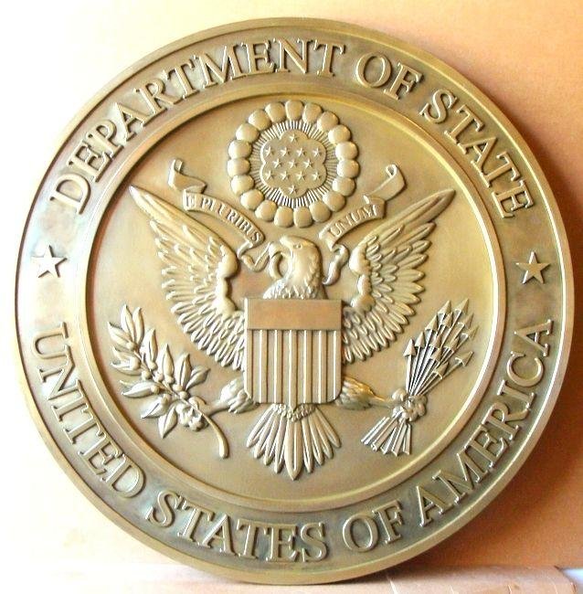 Close-up of a gold embossed seal of the U.S. Department of State with an eagle holding an olive branch and a bundle of arrows, and a shield on its chest, surrounded by stars.