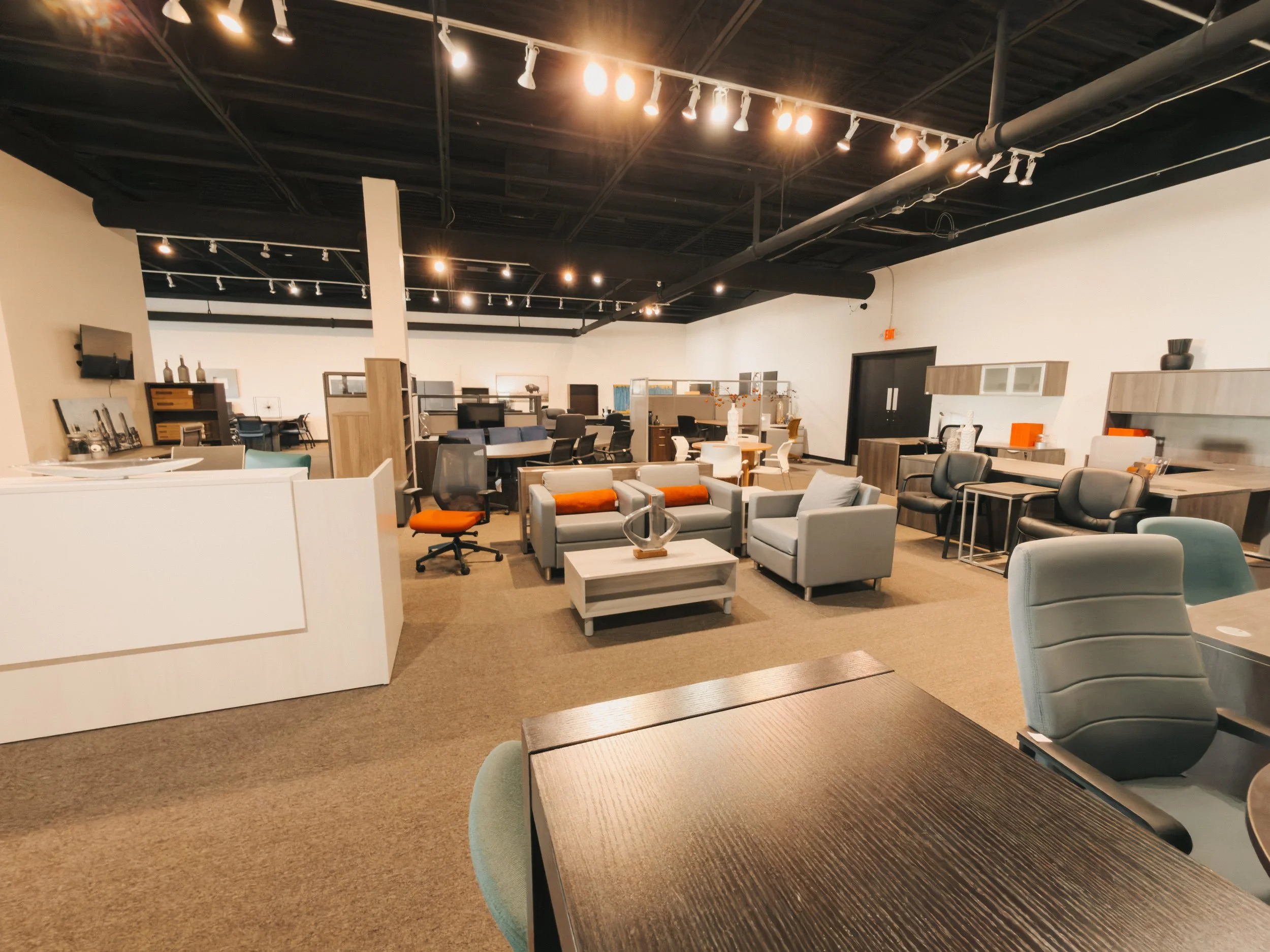 Crown Office Furnishings showroom floor with executive desks, reception counter, lounge seating area, cubicle systems, and storage cabinets under industrial track lighting