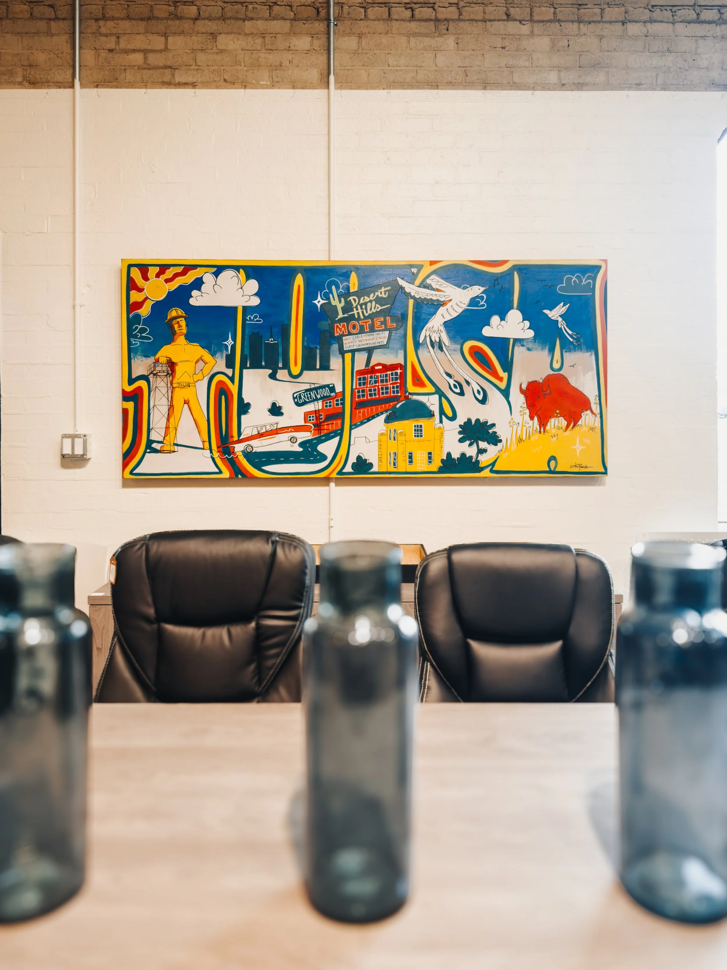 Conference room with black leather high-back chairs, wood table, and colorful Tulsa Oklahoma mural featuring the Golden Driller, Route 66, and state landmarks
