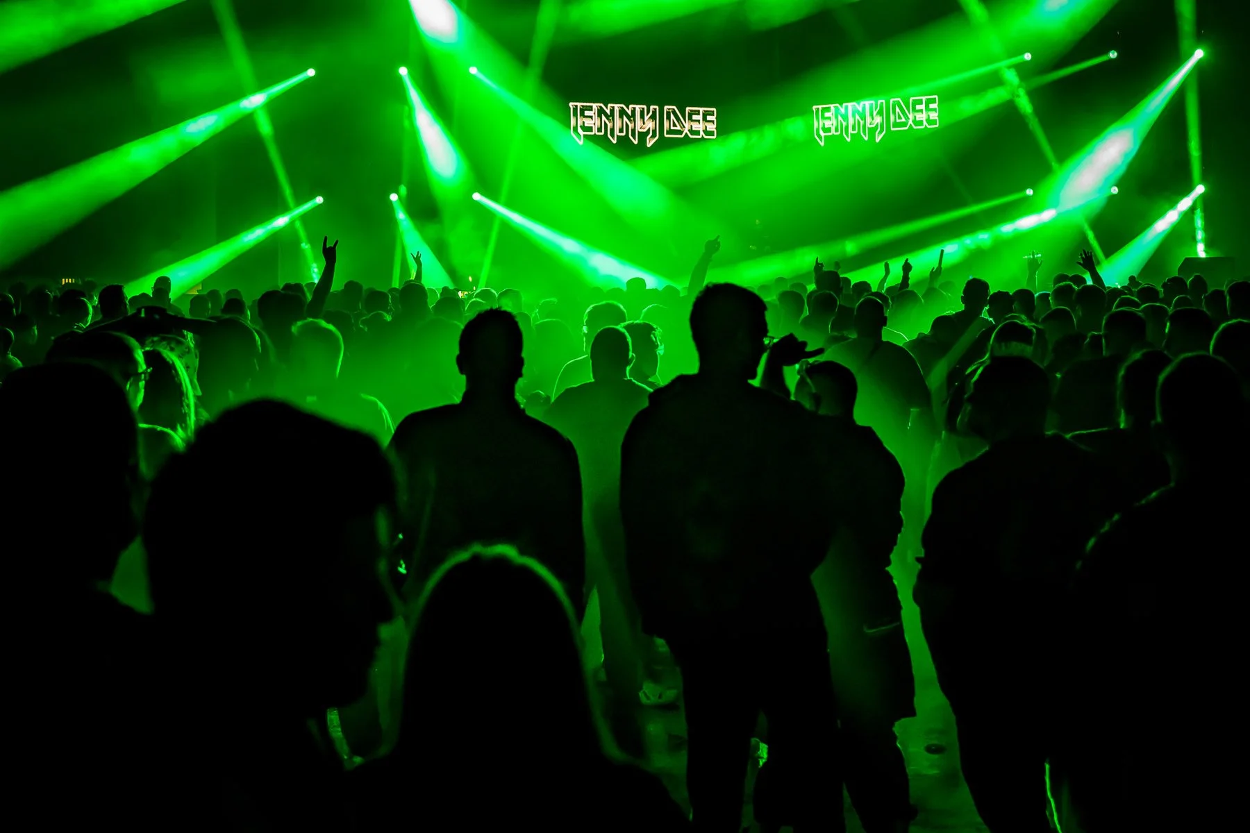 Concert crowd facing a stage with green lighting and the name 'Jenny Dee' displayed.