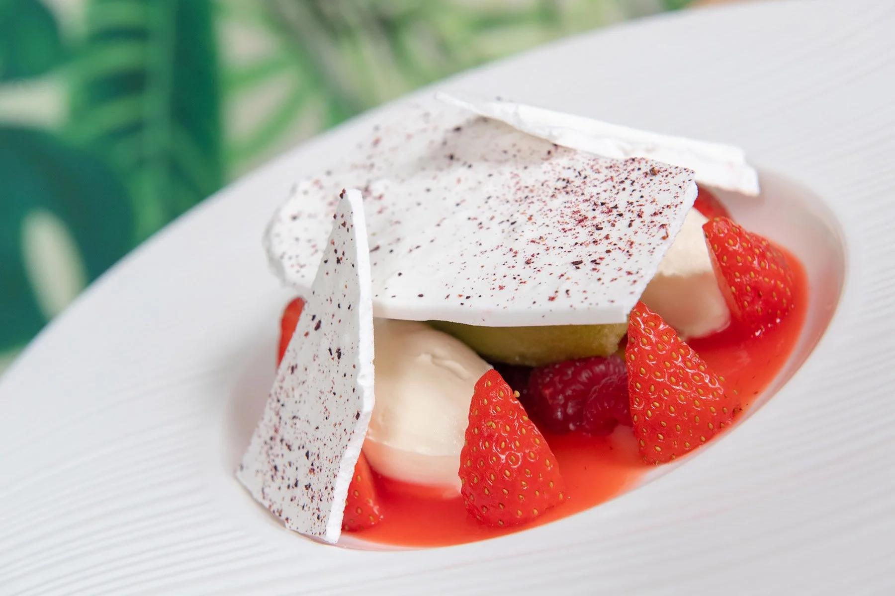 A dessert with strawberries, raspberries, and cream topped with white chocolate shards and a dusting of cocoa powder