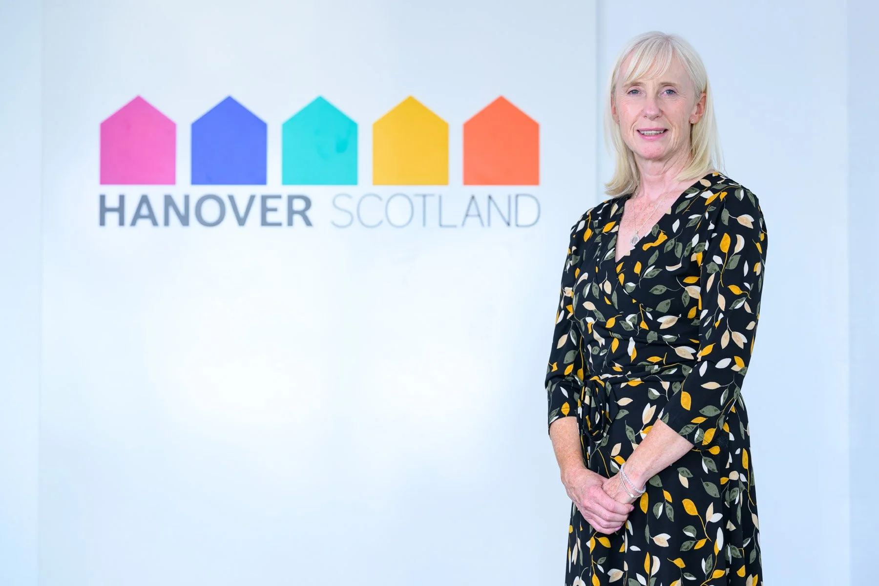 A woman standing in front of a logo that says "Hanover Scotland" with colorful house shapes.