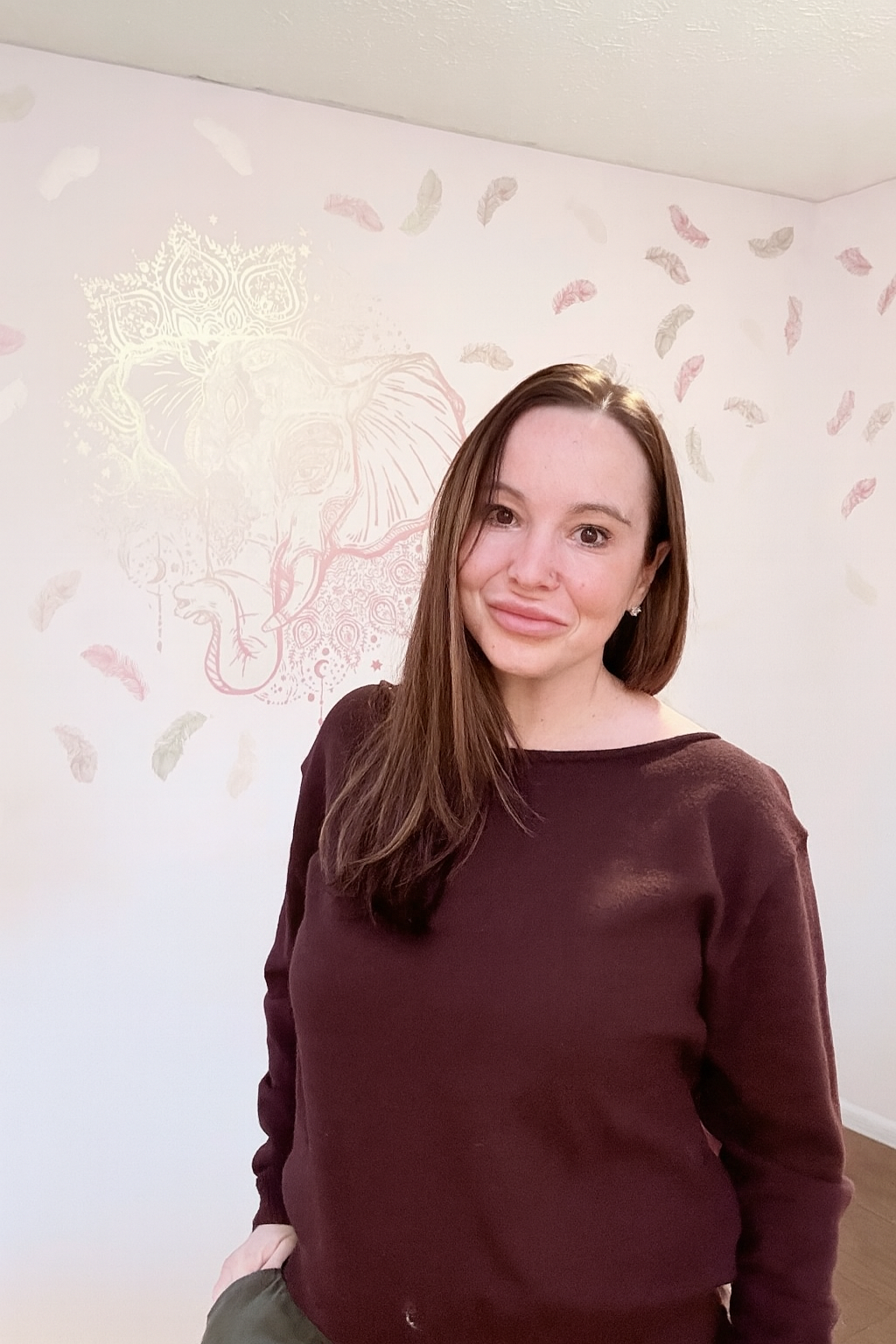 Heidi Forsman, intuitive reader, standing indoors with a feather-patterned background, offering energy insight and intuitive guidance.