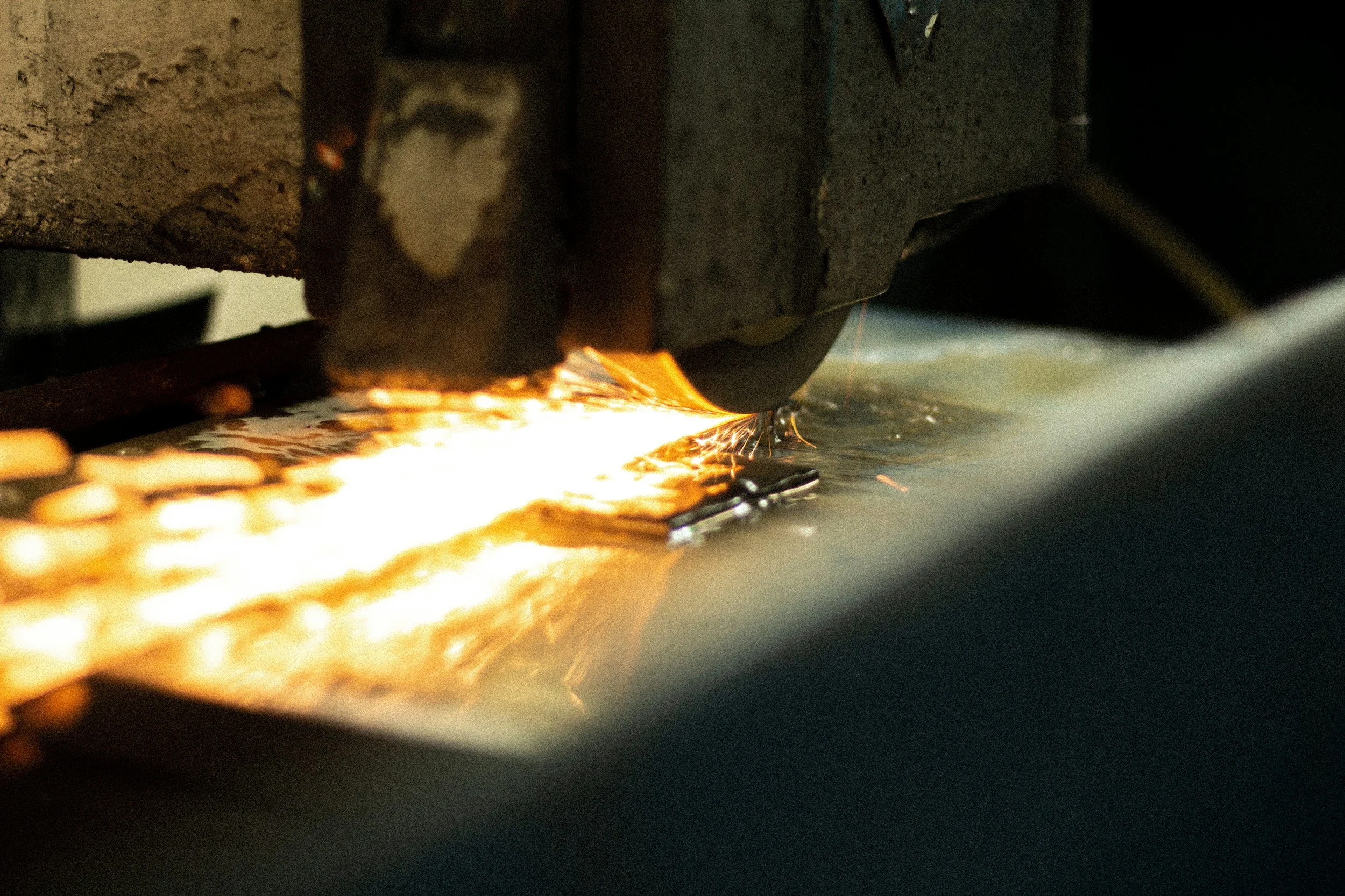 A metal-cutting machine sparks as it cuts through a piece of metal.