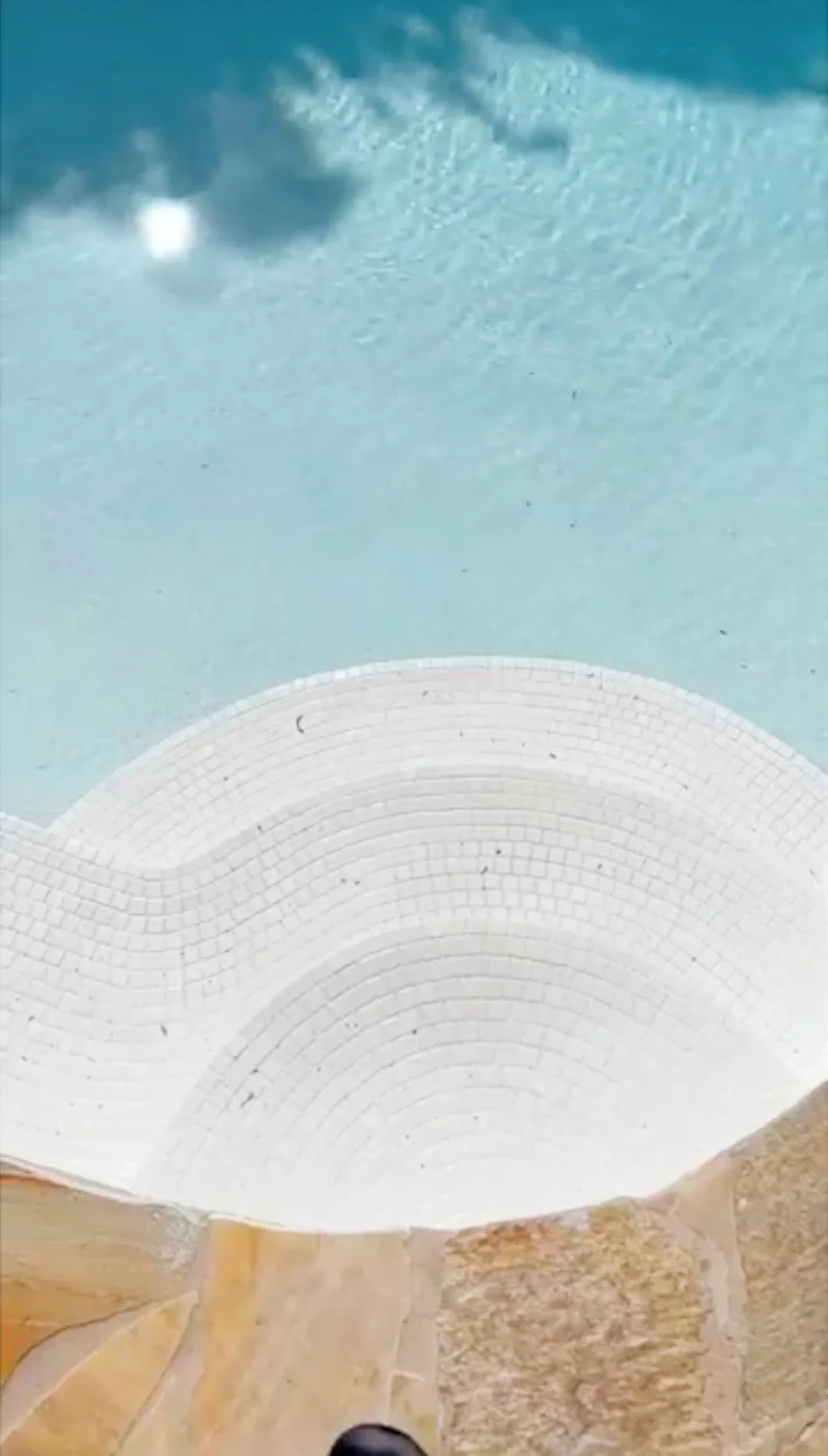 Close-up view of a white, curved architectural structure with tiled pattern, against a light blue sky with some clouds.