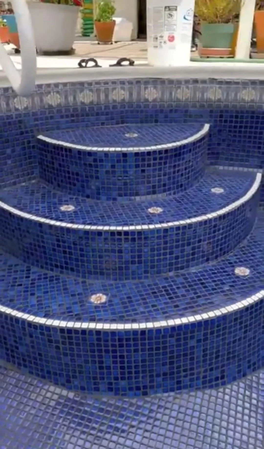 Blue tiled hot tub with three circular steps leading into the water.