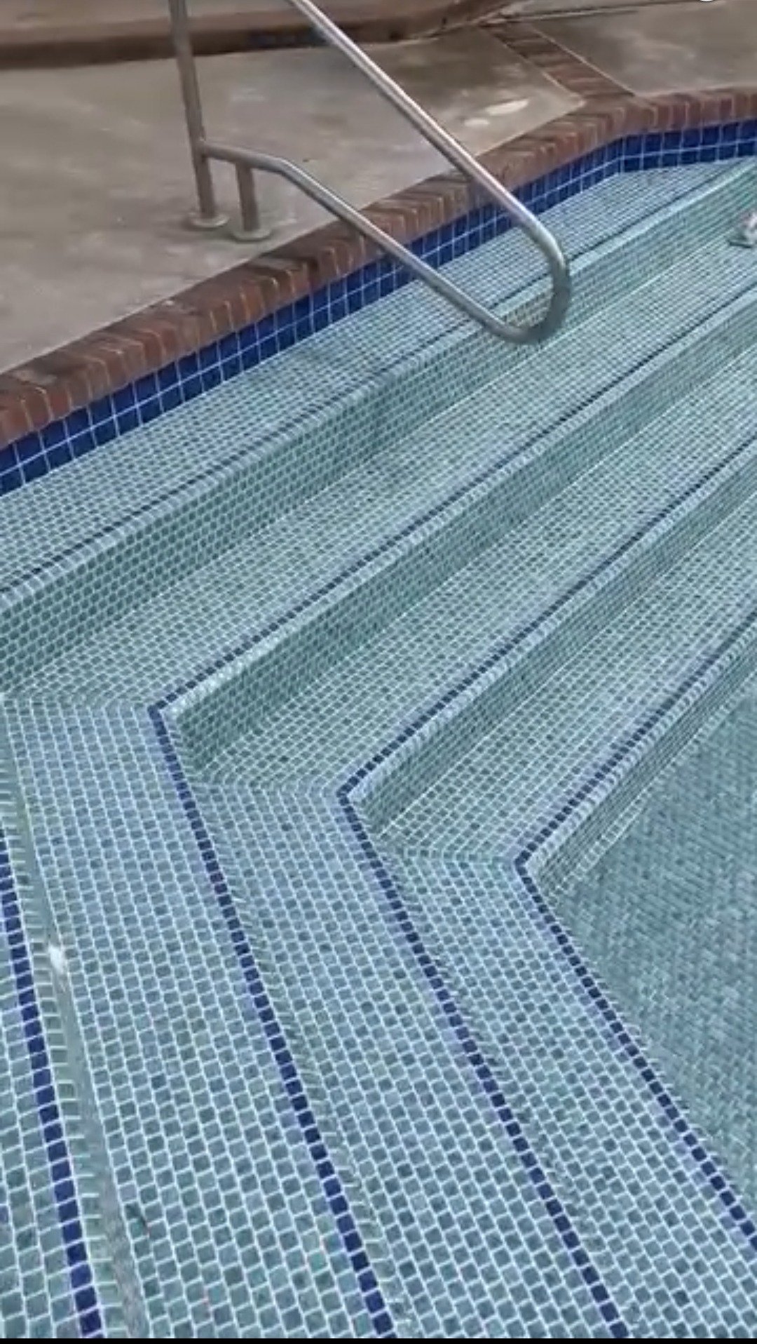 Close-up of tiled pool steps with metal handrails.