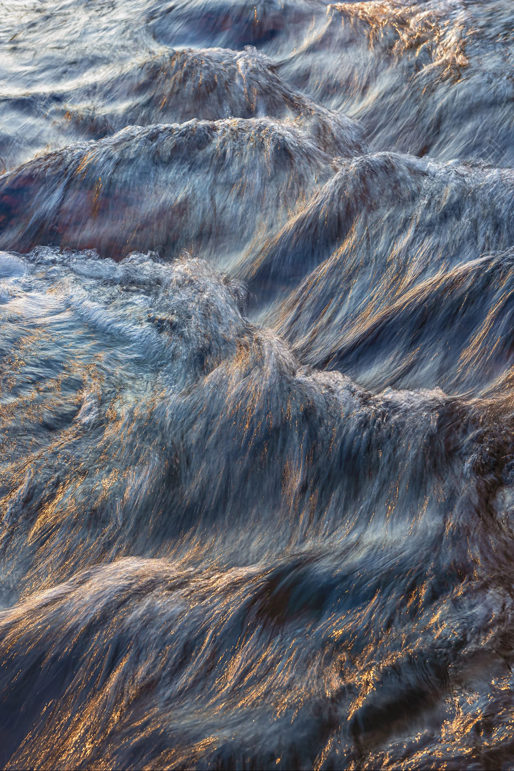 Close-up image of rushing water with golden lines of sunlight reflecting off water splatters