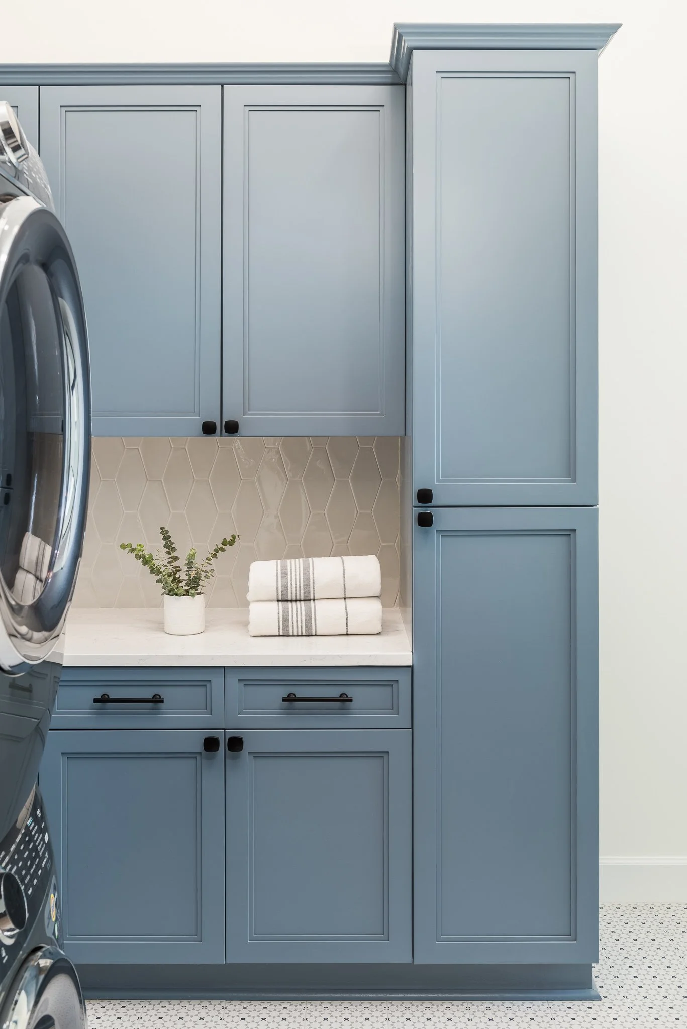 Blue laundry room cabinet with countertop, a potted plant, and folded towels, with washing machines on the left.
