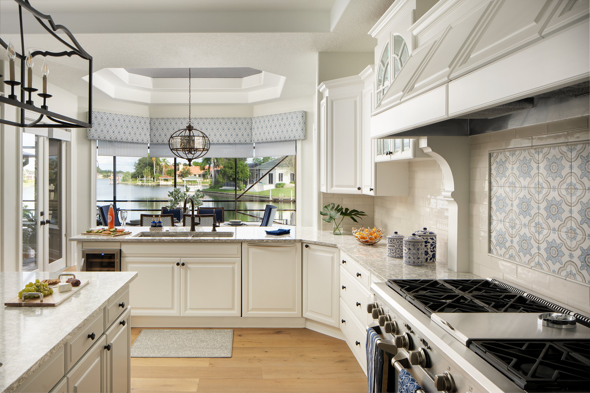 Bright kitchen with white cabinets and a view of a backyard waterway through large windows, featuring a kitchen island with a dual sink and decorative items.