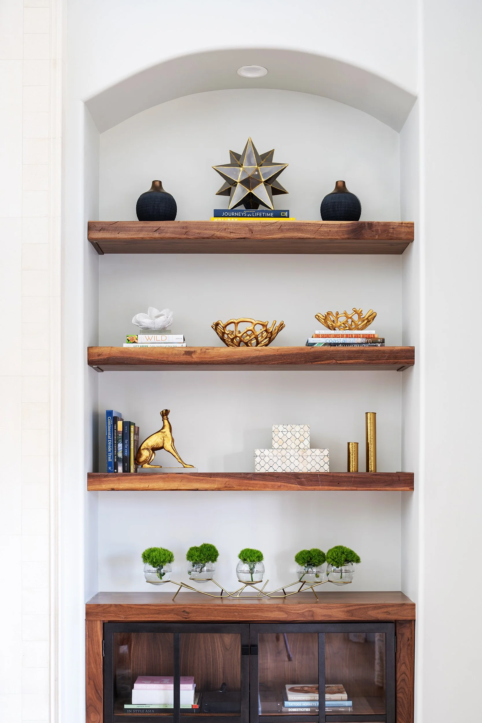Decorative shelving unit with books, vases, gold figurines, and plants.