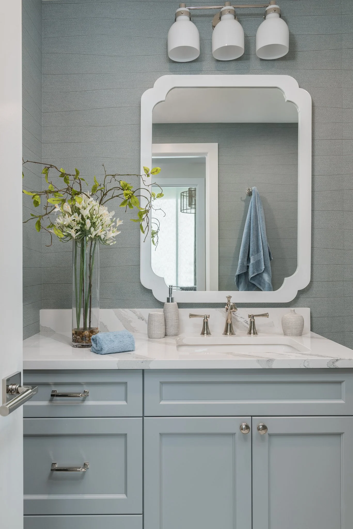 Bathroom vanity with a large mirror, flower vase, and various toiletries on a marble countertop in a modern bathroom.