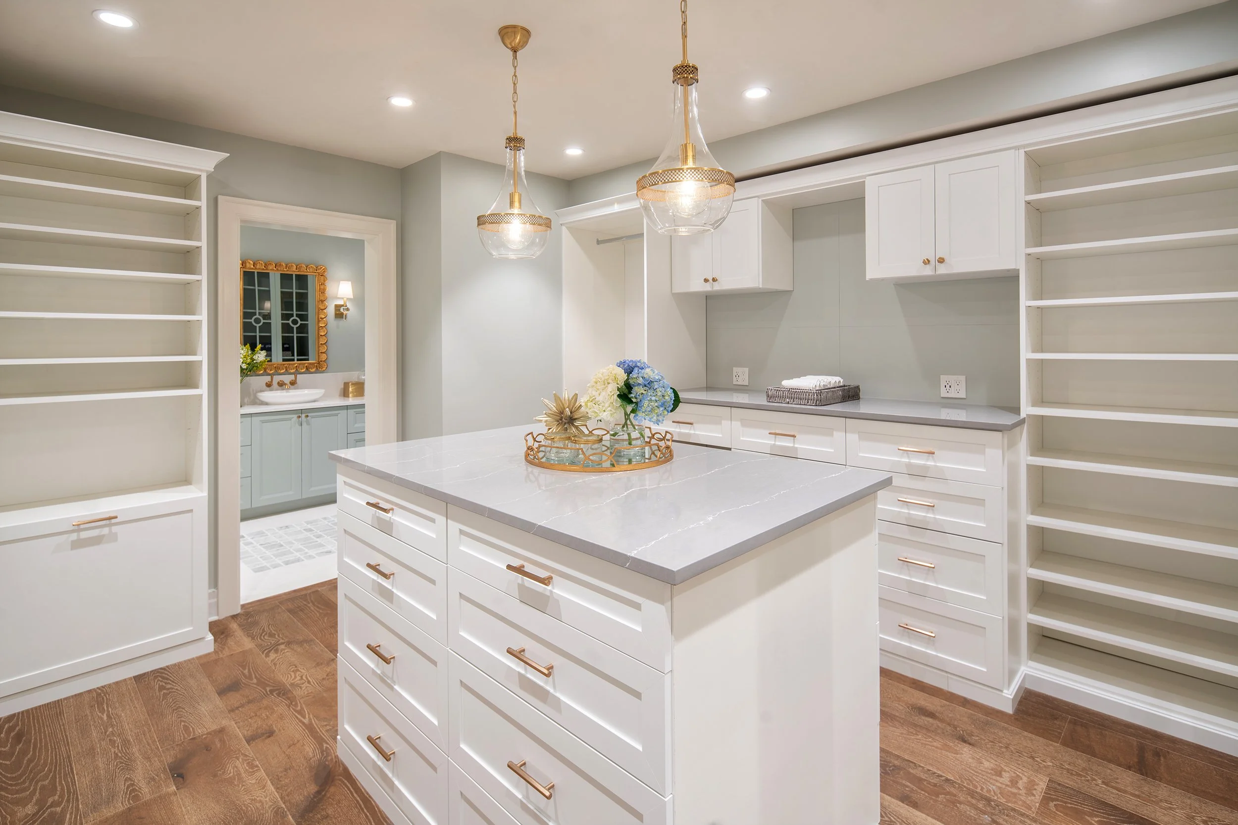 Modern kitchen with white cabinetry, marble countertop island, and built-in shelves, with hanging pendant lights and hardwood floors.