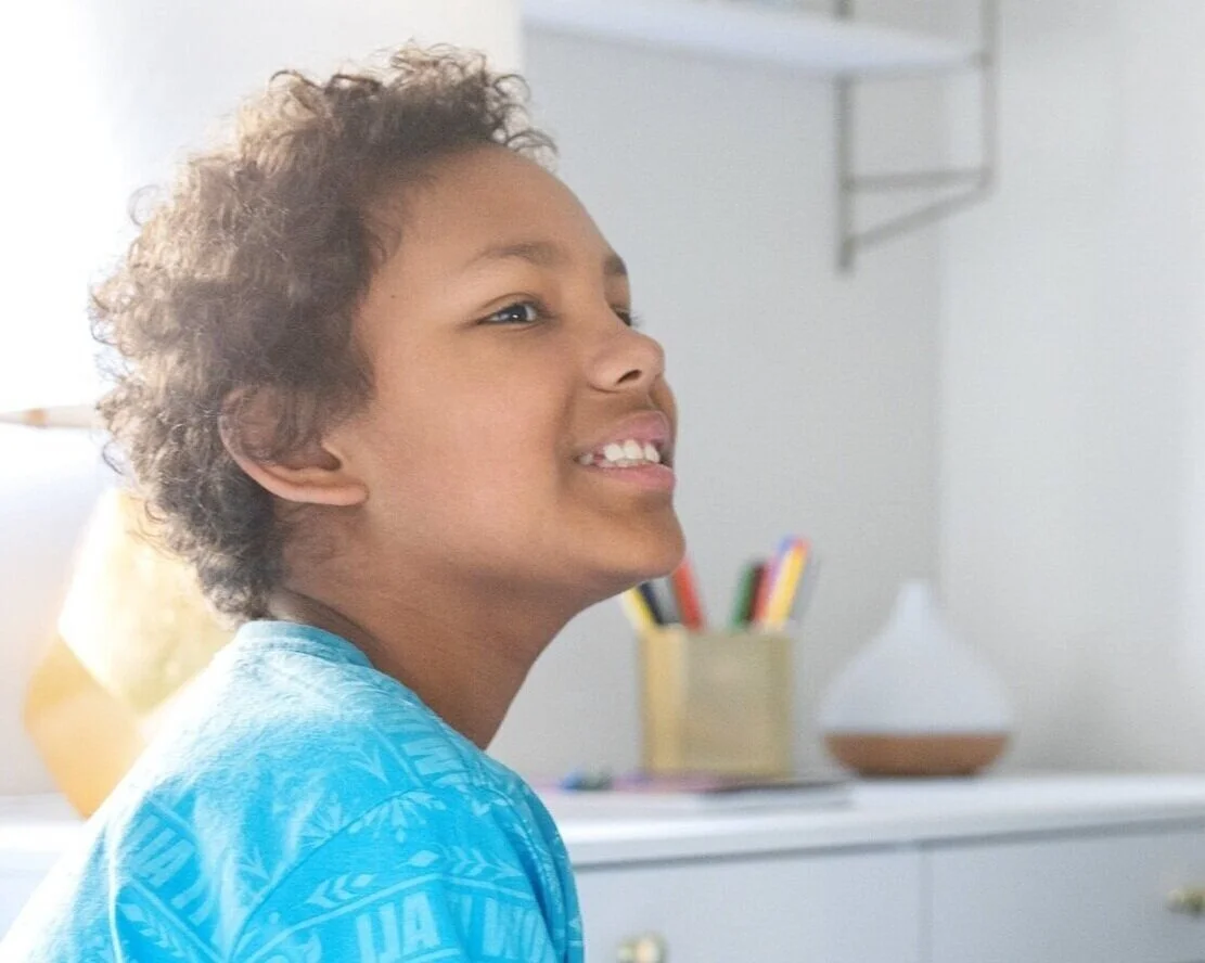A young boy with curly hair smiling in a bright room.