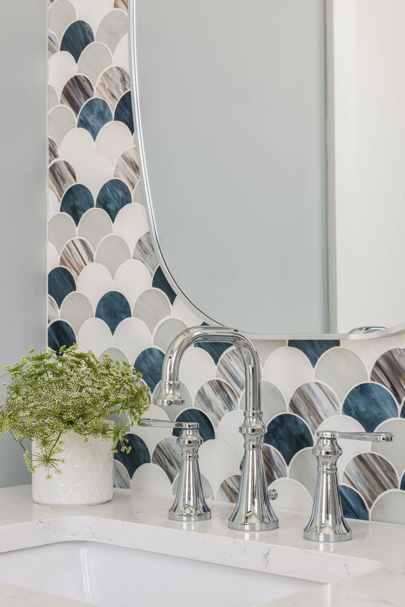 Close-up of a bathroom sink with a modern faucet, a mirror, and decorative tile backsplash, along with a potted plant on the countertop.