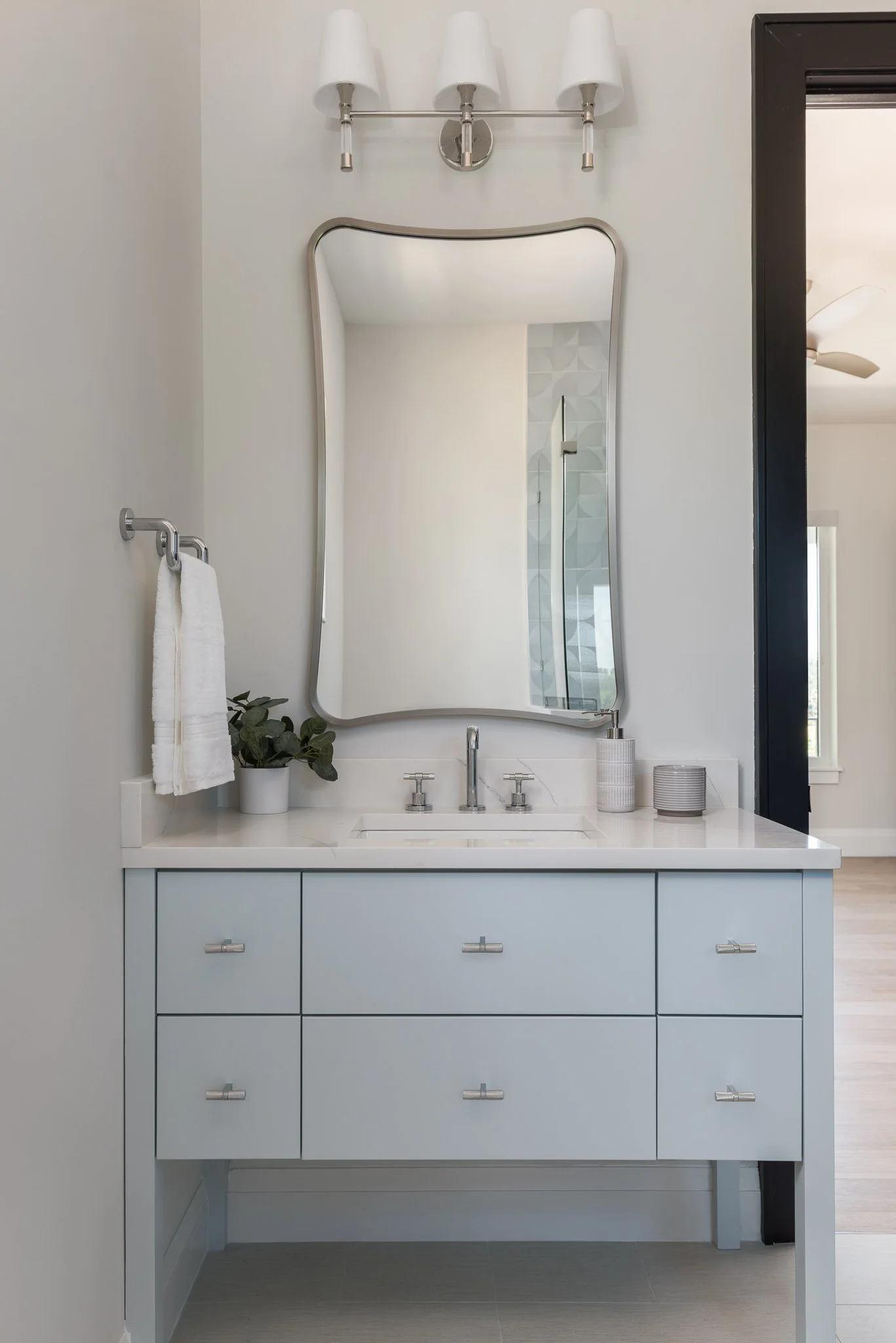 Modern bathroom vanity with a light blue cabinet, white countertop, and a large mirror, complemented by a wall-mounted light fixture and decorative items.