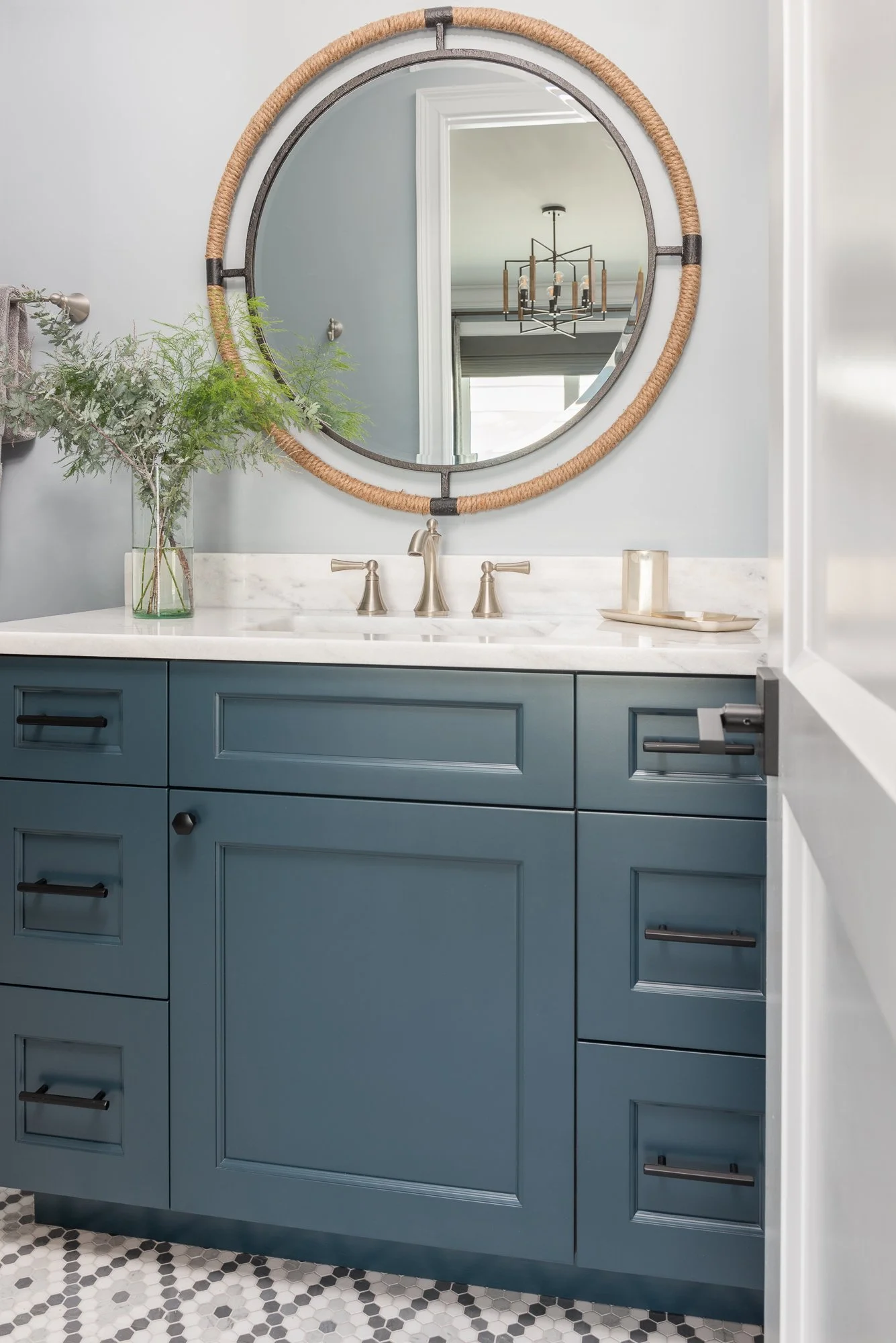 Bathroom vanity with a blue cabinet, white marble countertop, and a round mirror above it, reflecting a light fixture.