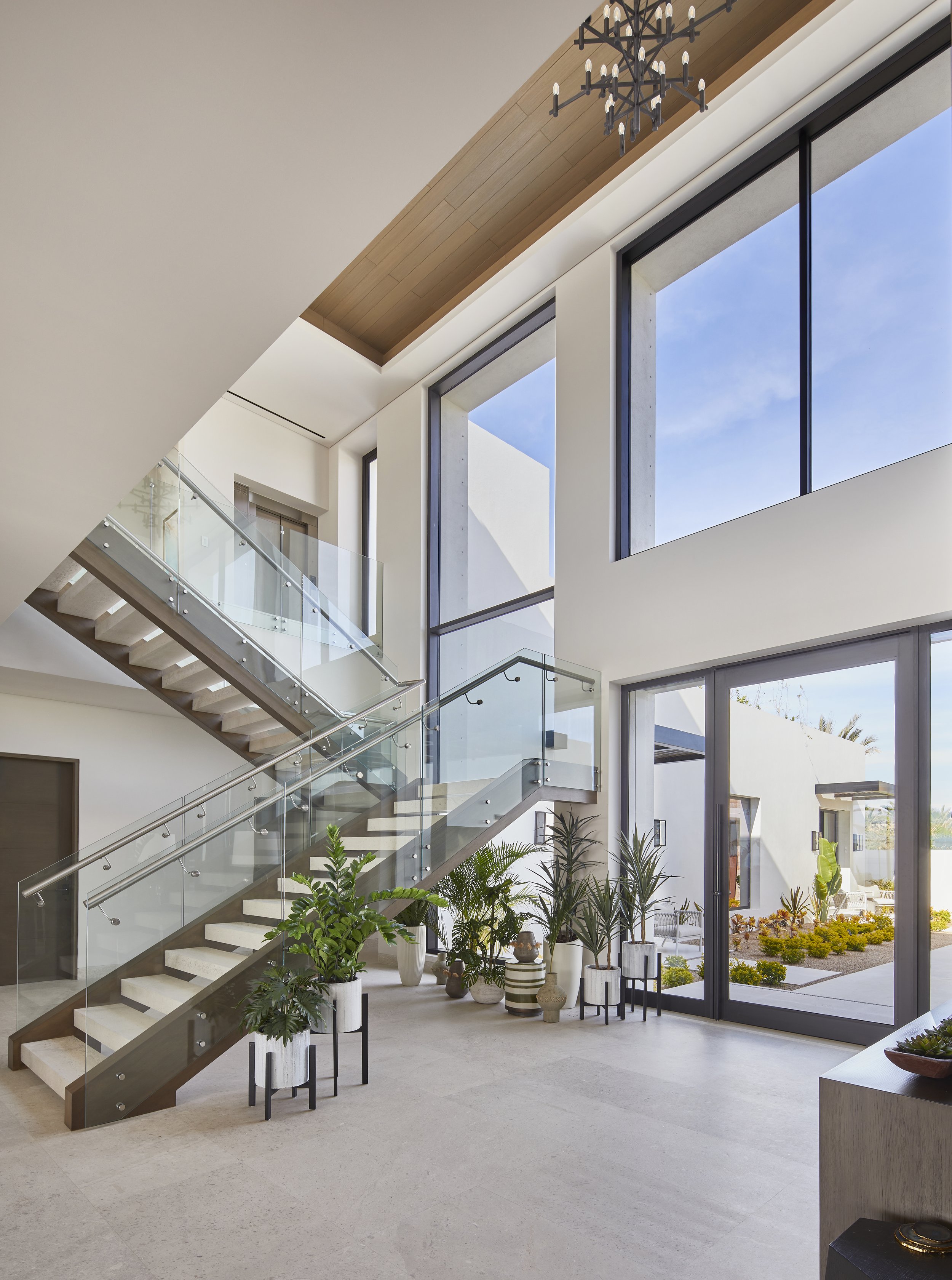 Modern interior with a staircase, large windows, and potted plants in a spacious, well-lit room.
