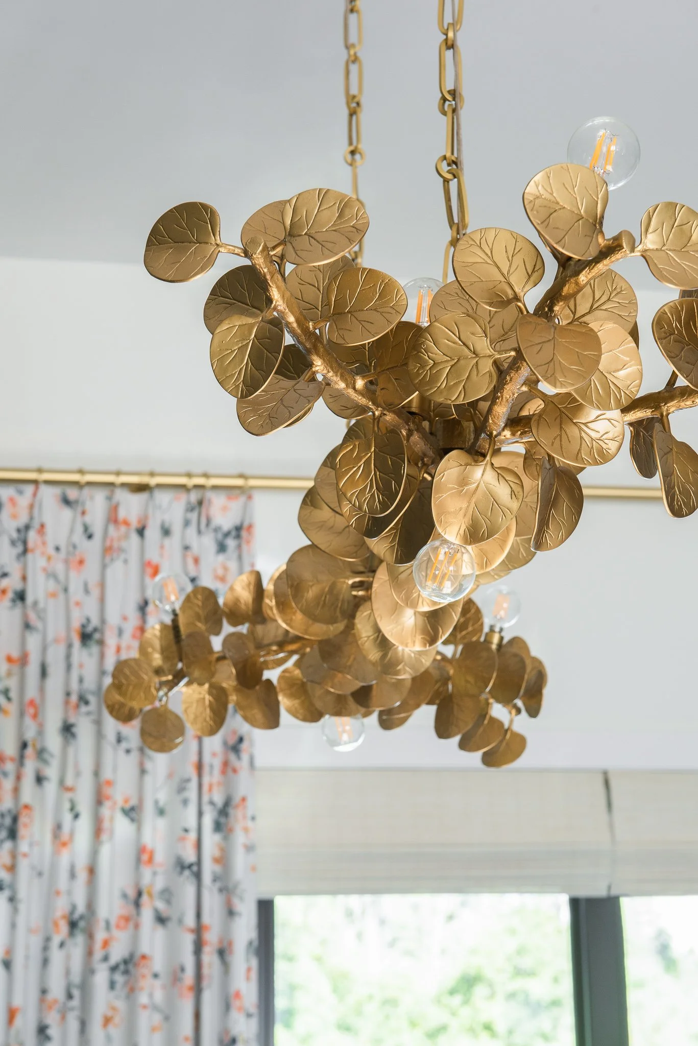 Gold-colored chandelier with leaf-shaped decorations and light bulbs hanging from chains.