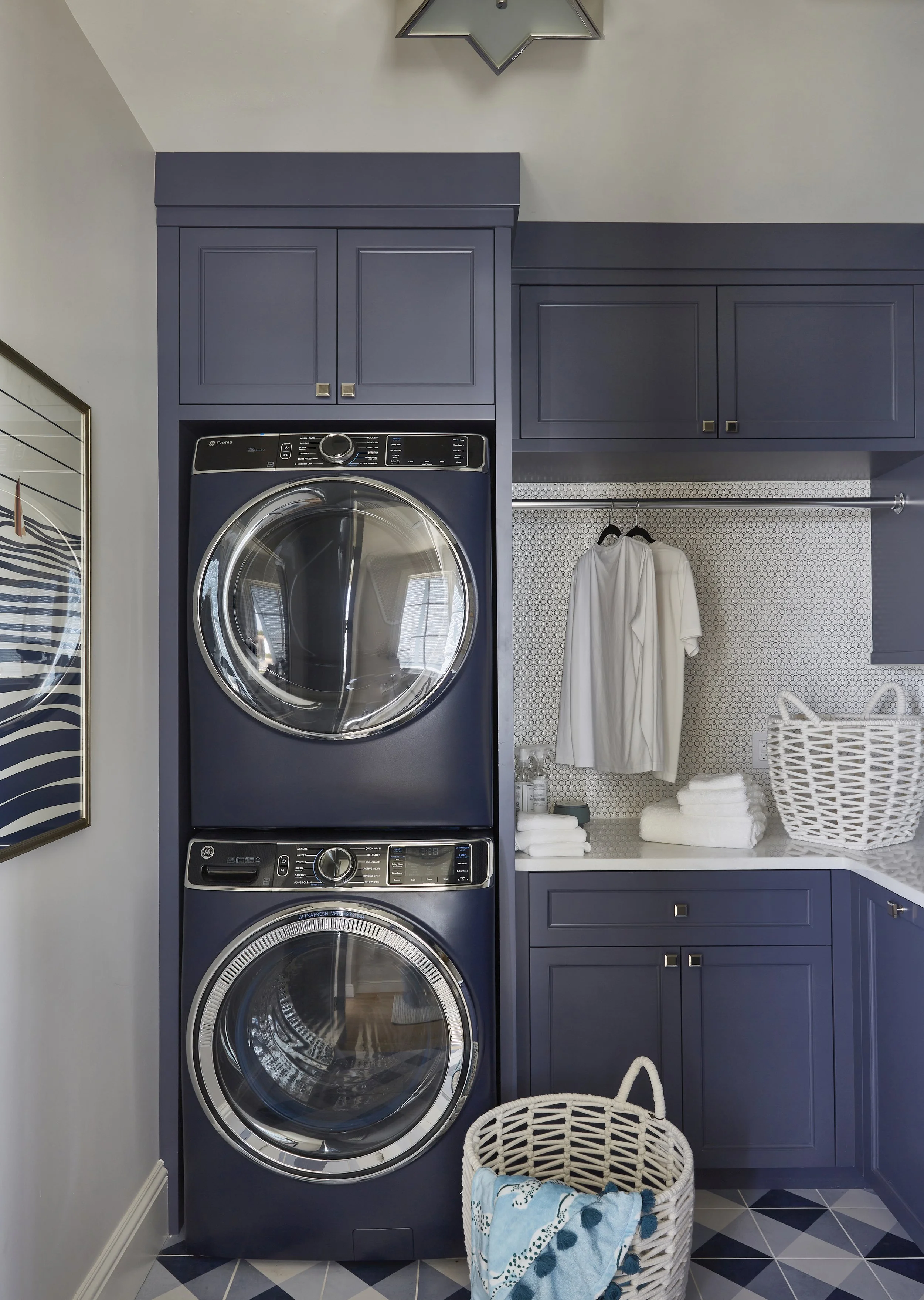 Stacked front-loading washer and dryer in a laundry room with navy blue cabinets, a laundry basket, and folded towels.