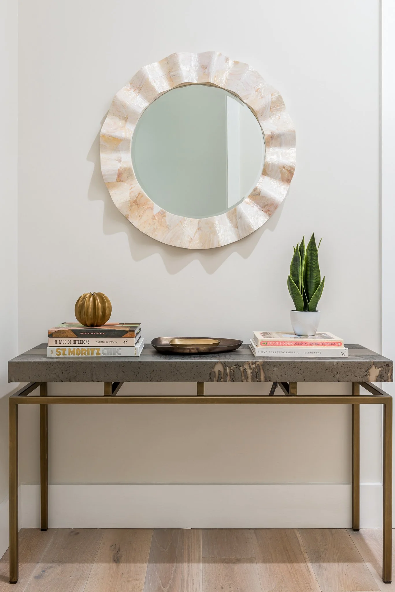 Decorative console table with books, a small pumpkin, a tray, and a potted plant against a wall with a round mirror.